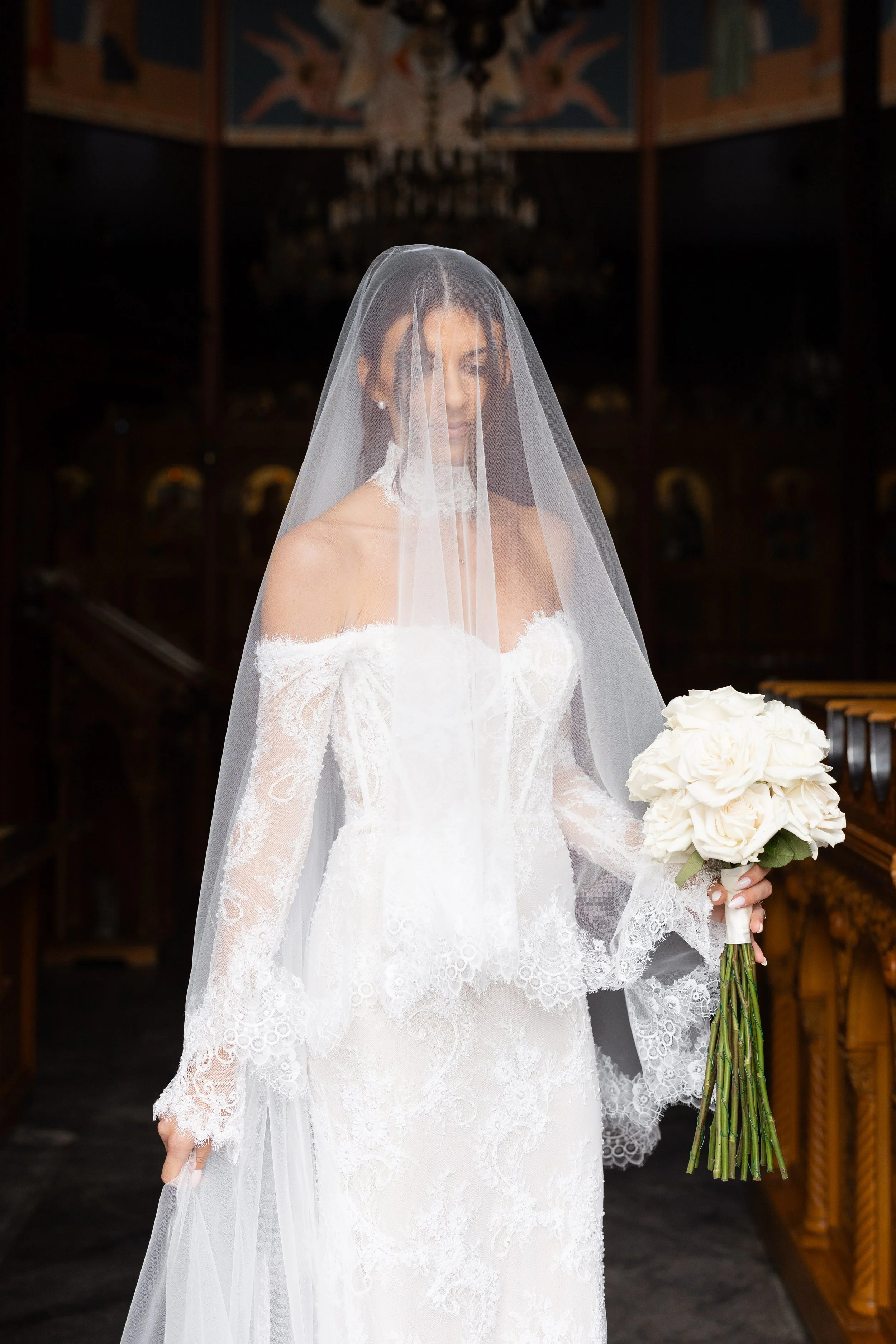 Steph in her veil and lace gown holding a white bouquet inside the church