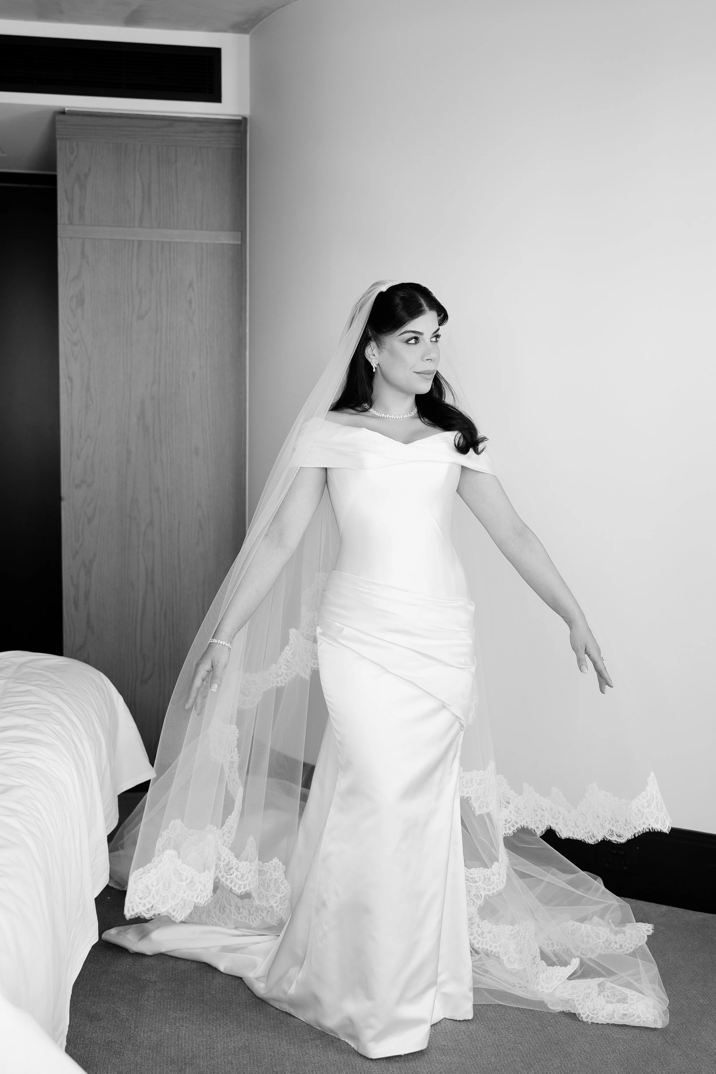 Jihan walking in a long veil and off-the-shoulder gown, in black and white
