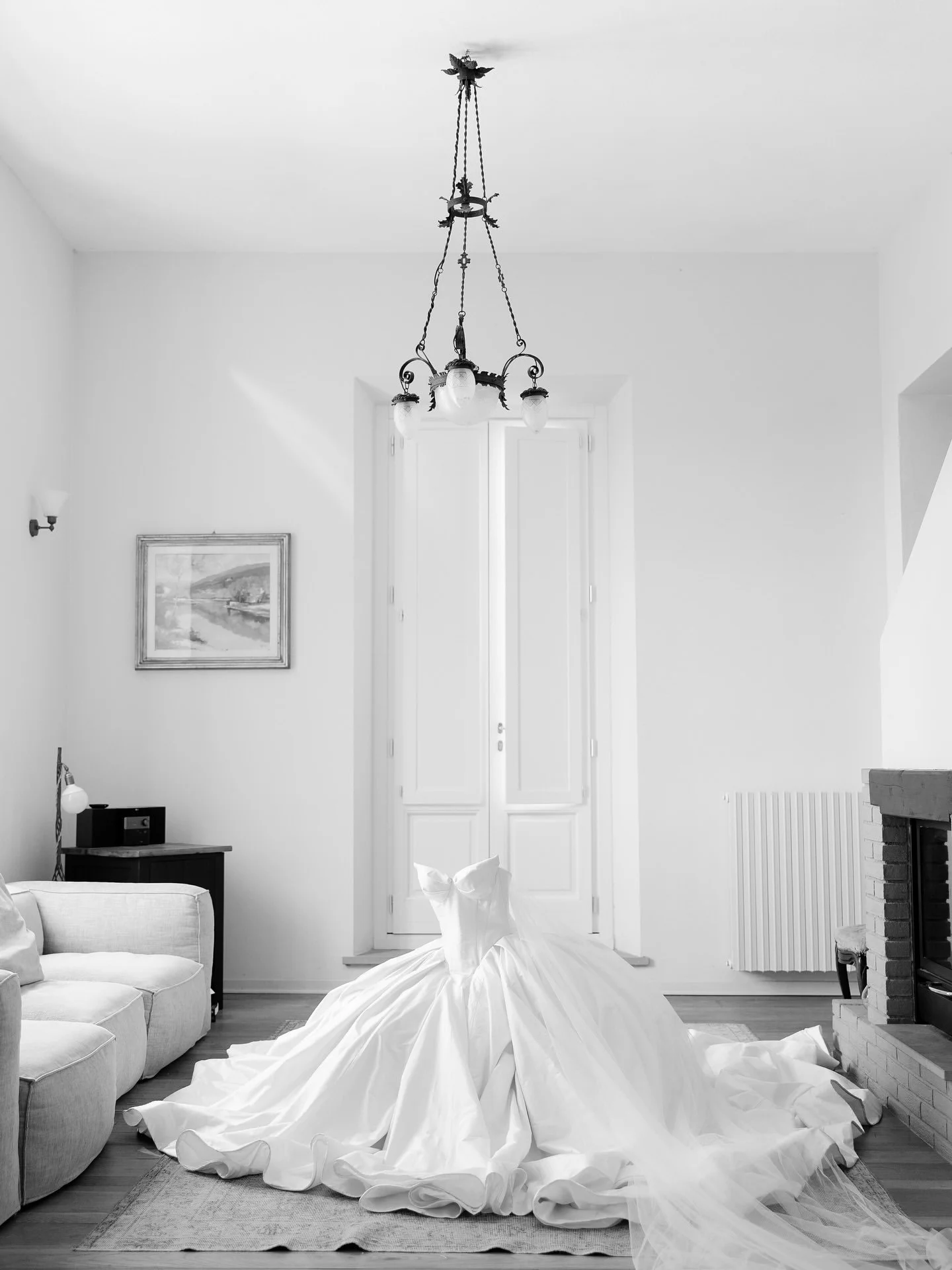 Black and white photo of a bride's gown in an elegant room with a chandelier