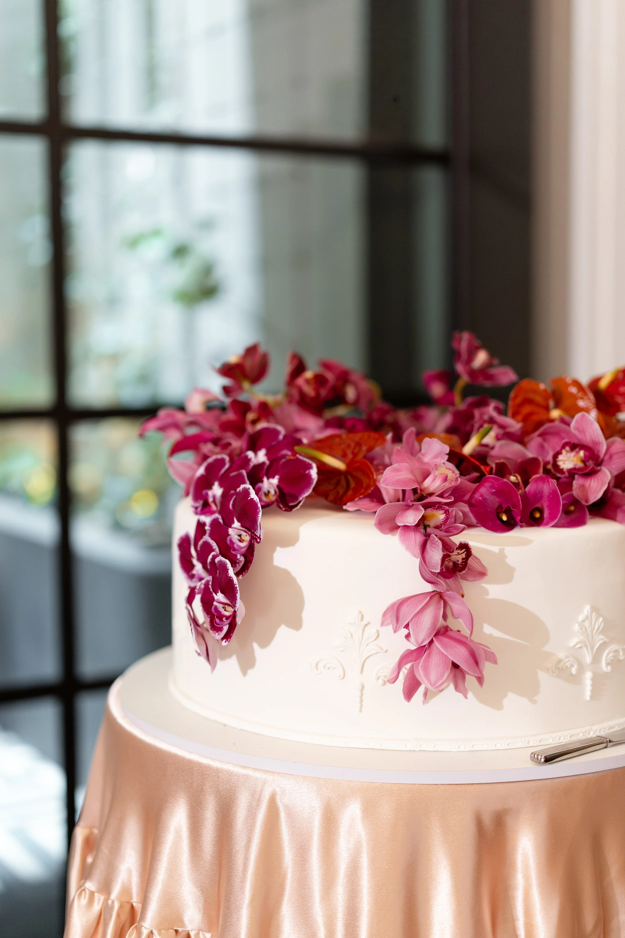 Jihan and Rob’s orchid-topped wedding cake on a peach silk table at Luci Melbourne