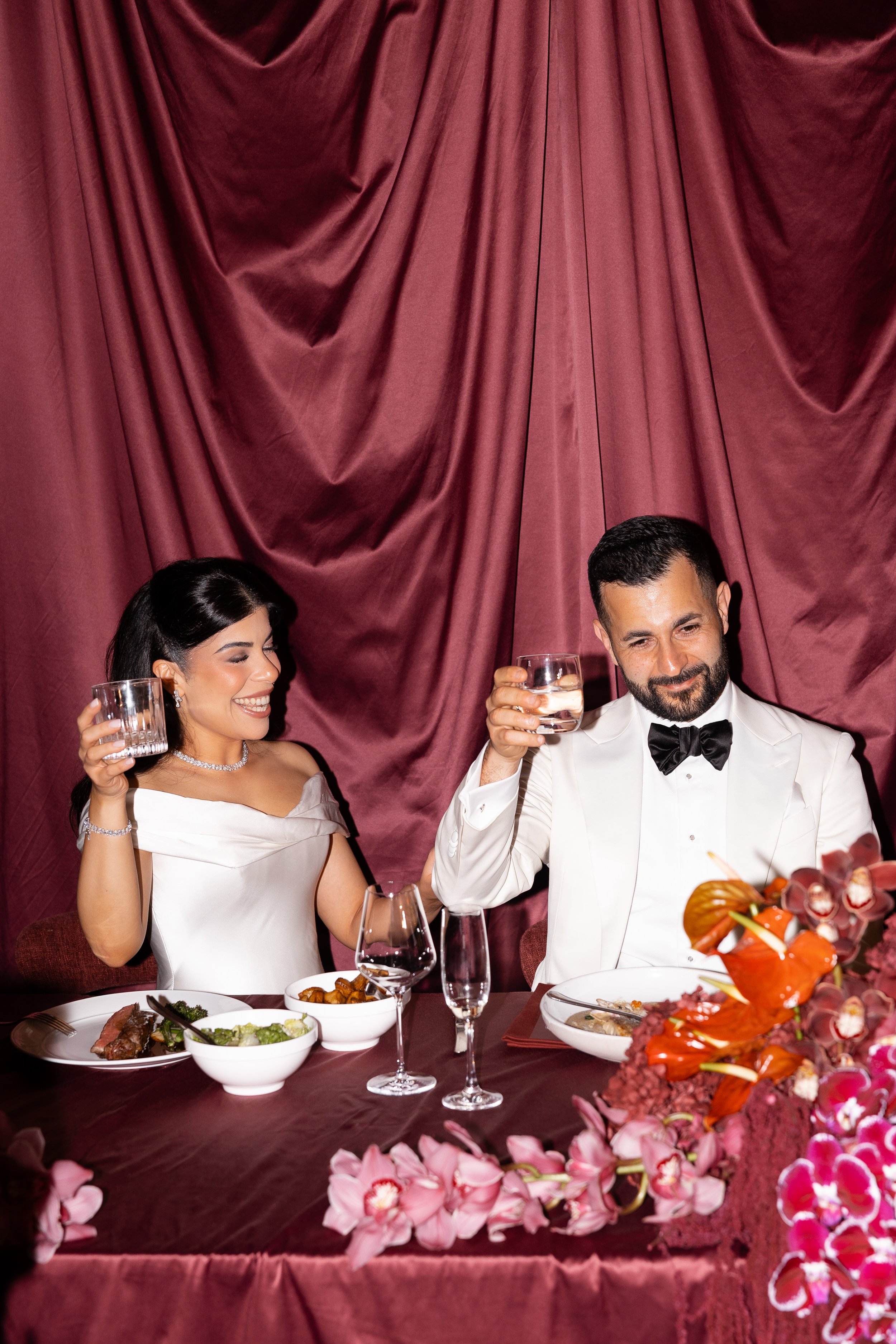 Jihan and Rob raising a toast at a burgundy-draped table at Luci Melbourne