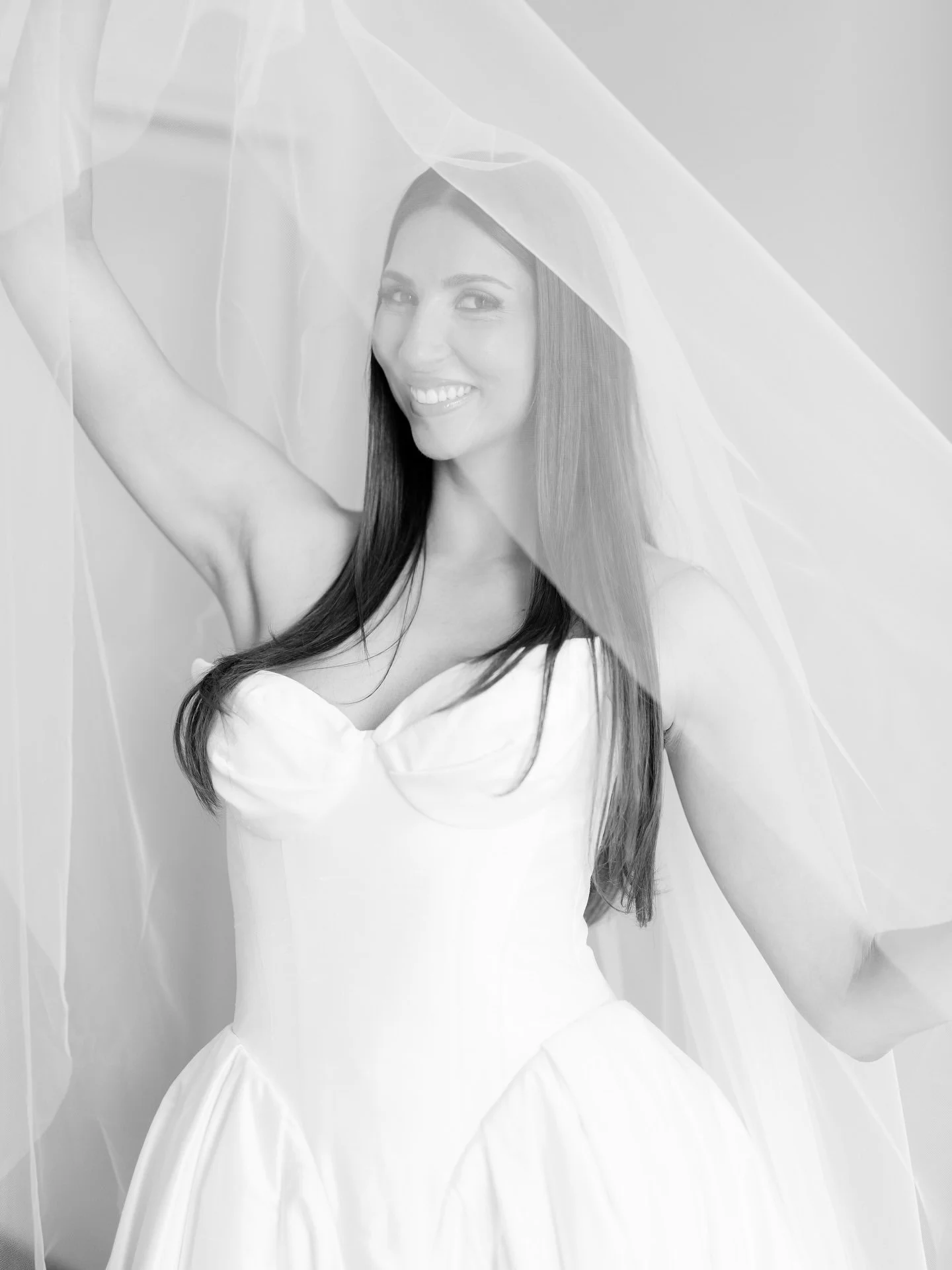 Black and white portrait of Marilena smiling in her veil with her arm raised