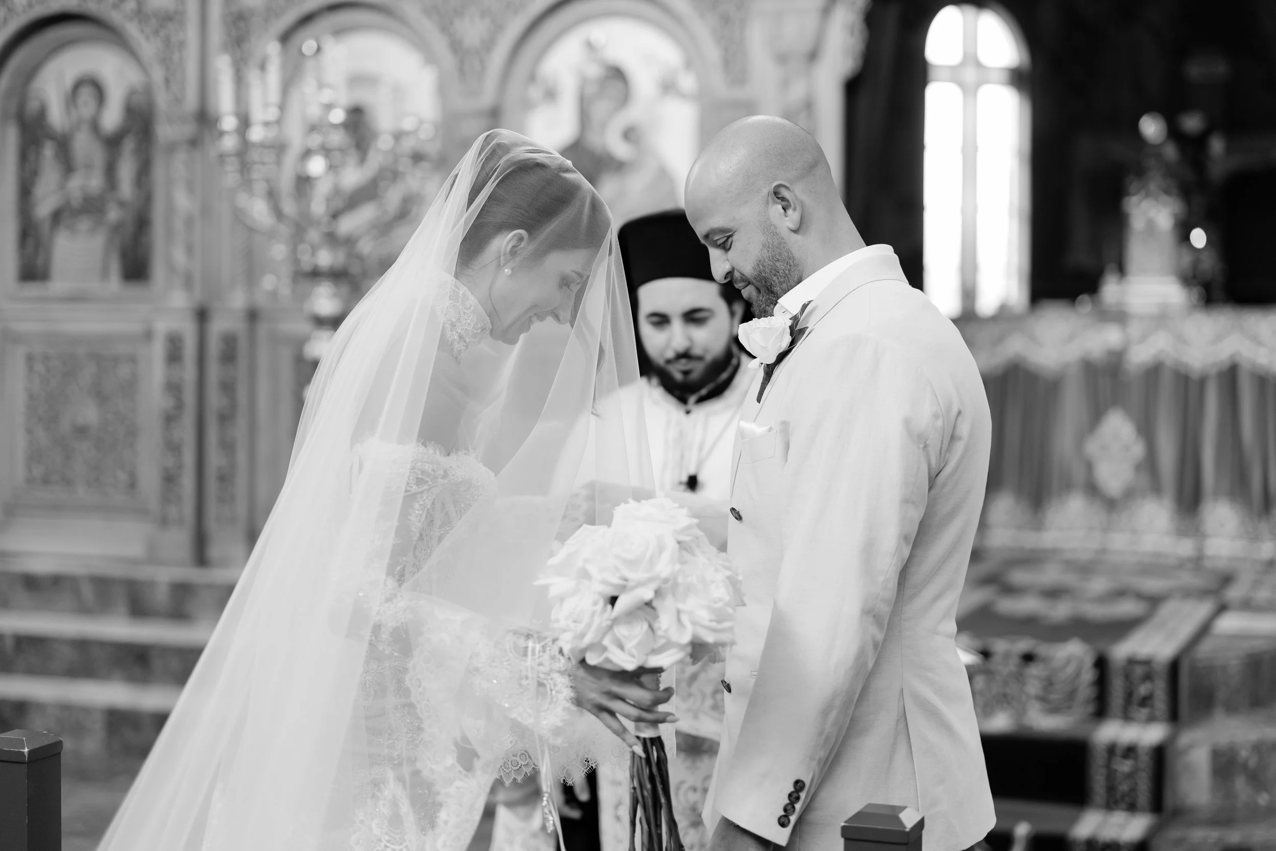 Steph and Alex ceremony in black and white, Steph in her long veil with a priest behind