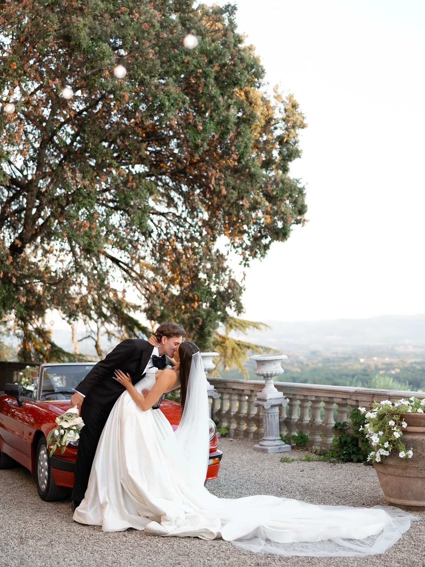 Bride and groom beside a tree with a view across the Tuscan hills