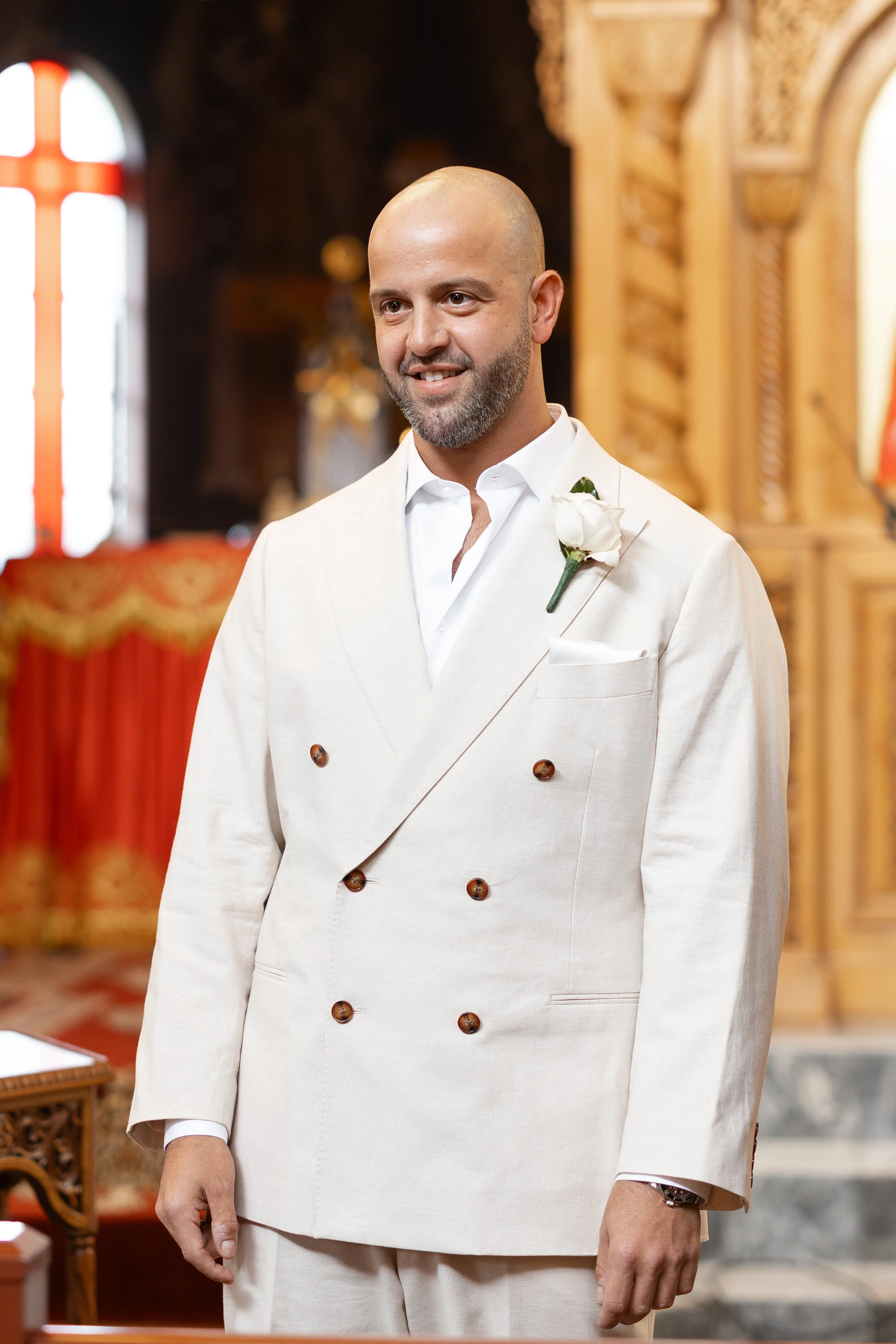Steph and Alex ceremony: Alex in a cream suit with a white boutonniere inside Holy Monastery of Panagia Kamariani