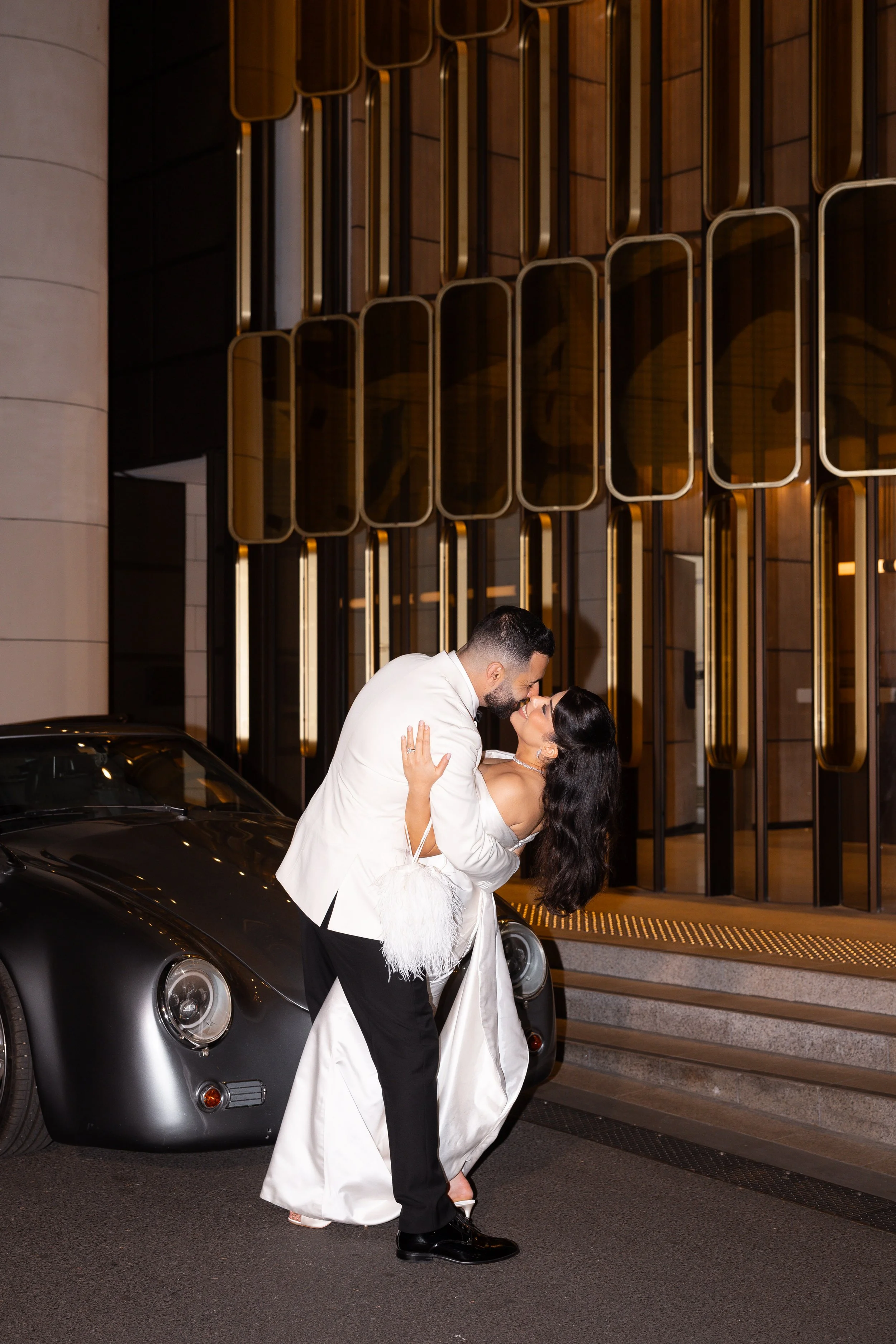 Jihan and Rob kissing beside a classic car outside the hotel at night