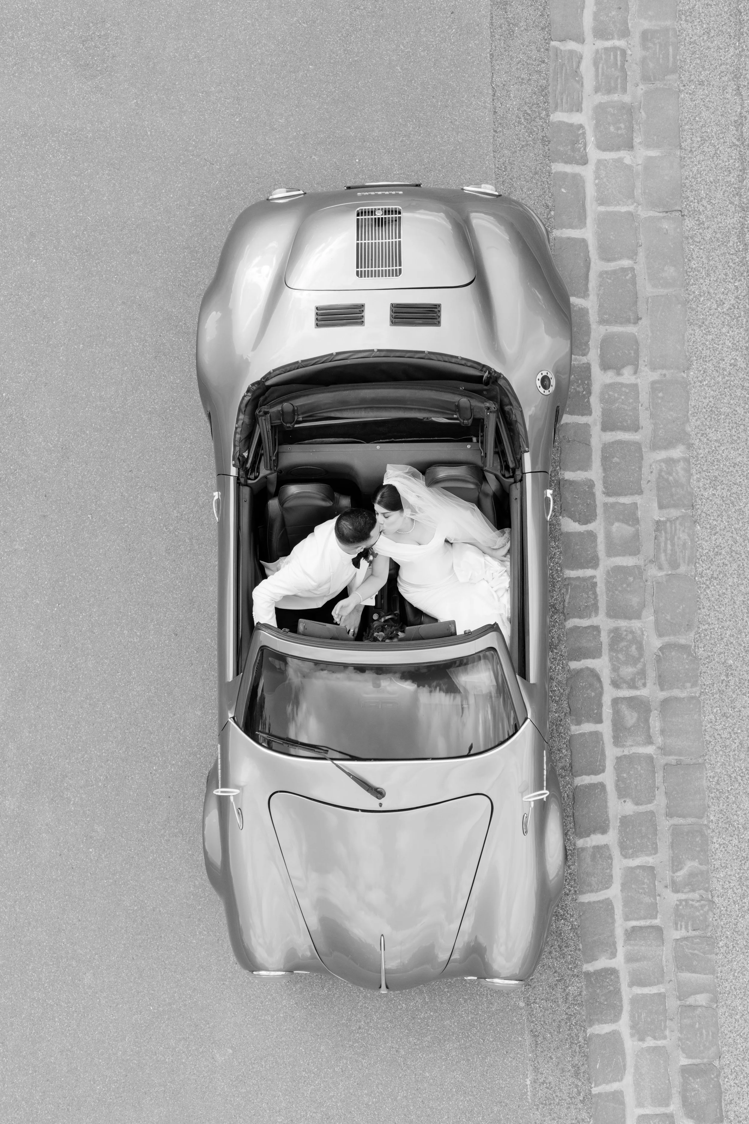 Jihan and Rob embracing in an open classic convertible, seen from above