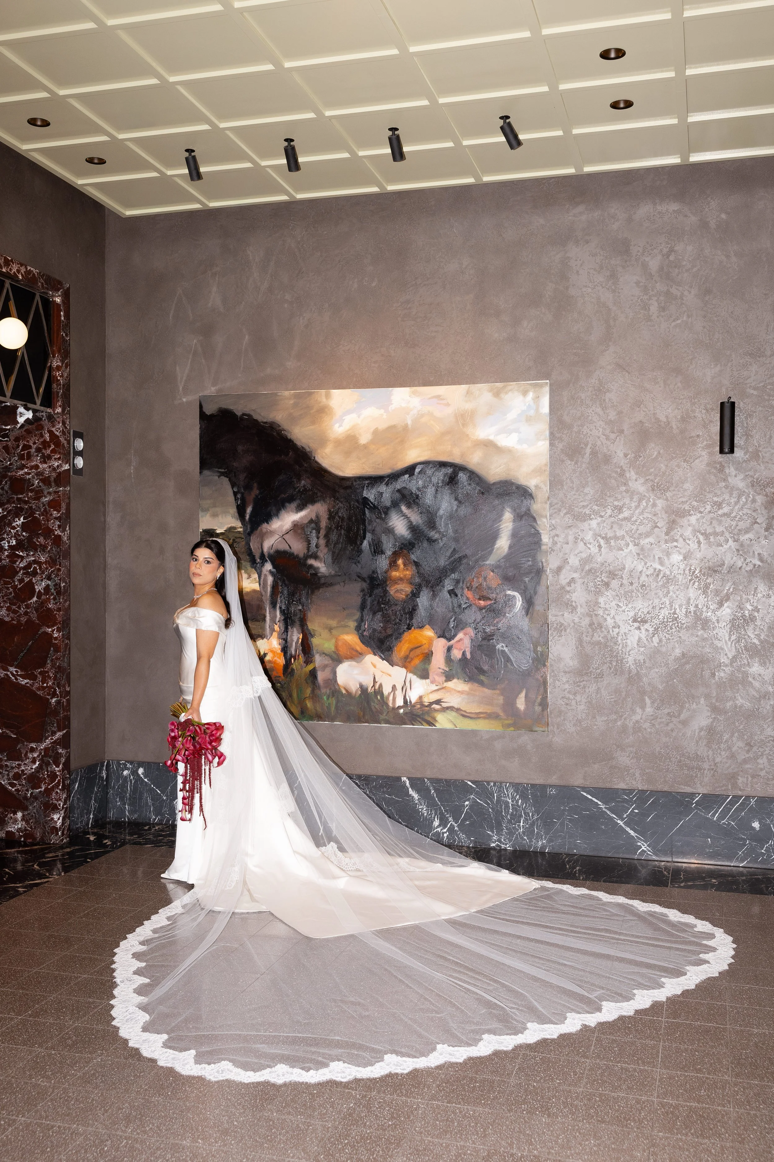 Jihan in a long lace-trimmed veil and gown by a fireplace in the hotel