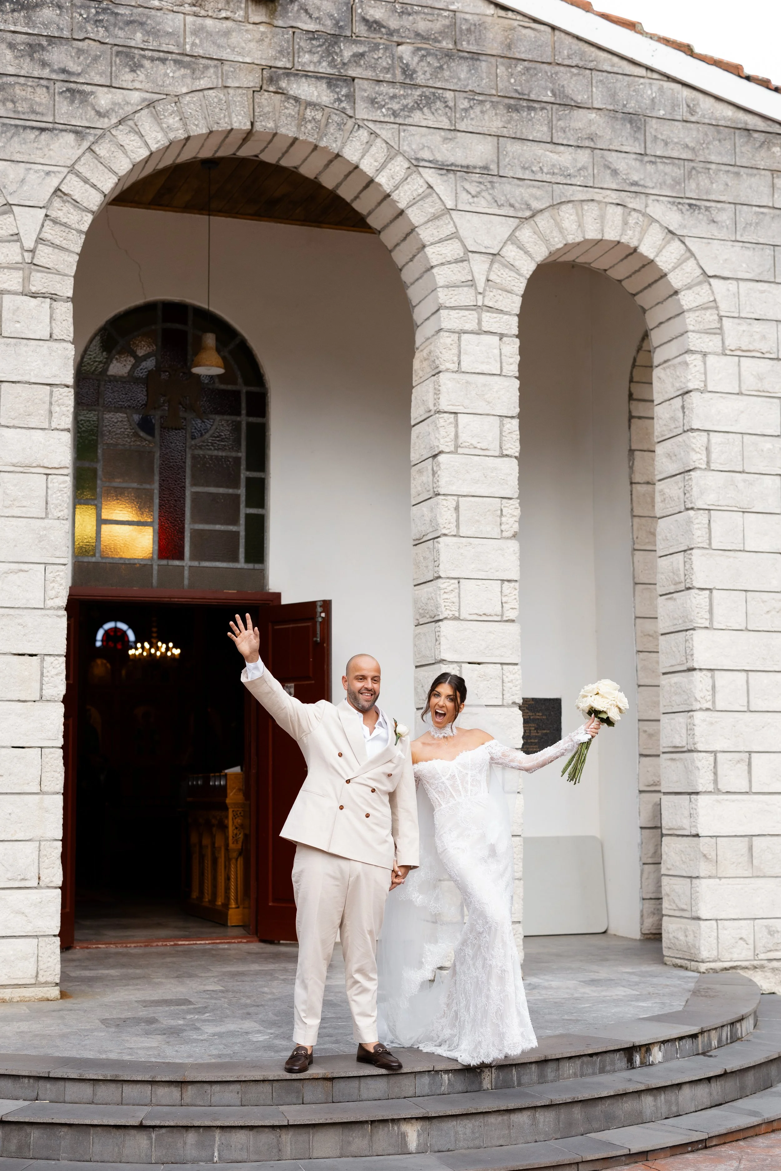 Steph and Alex raise their arms outside the stone church entrance