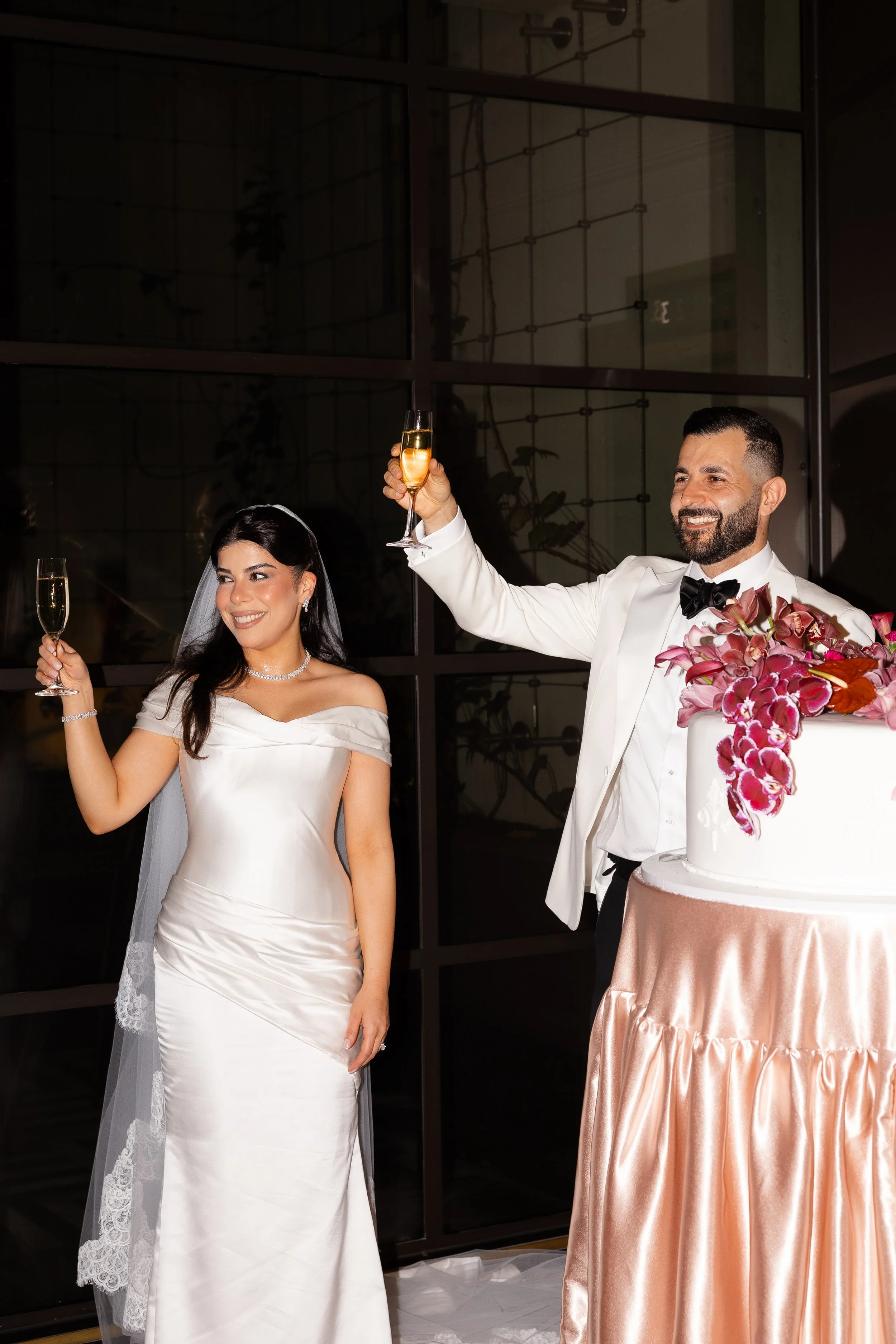 Jihan and Rob raising a toast beside their orchid-topped cake at Luci Melbourne