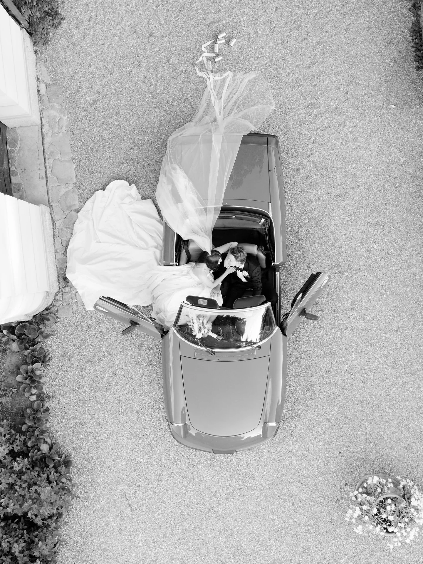 Black and white aerial photo of Marilena and Joshua in a vintage convertible at Villa Belvedere, Tuscany