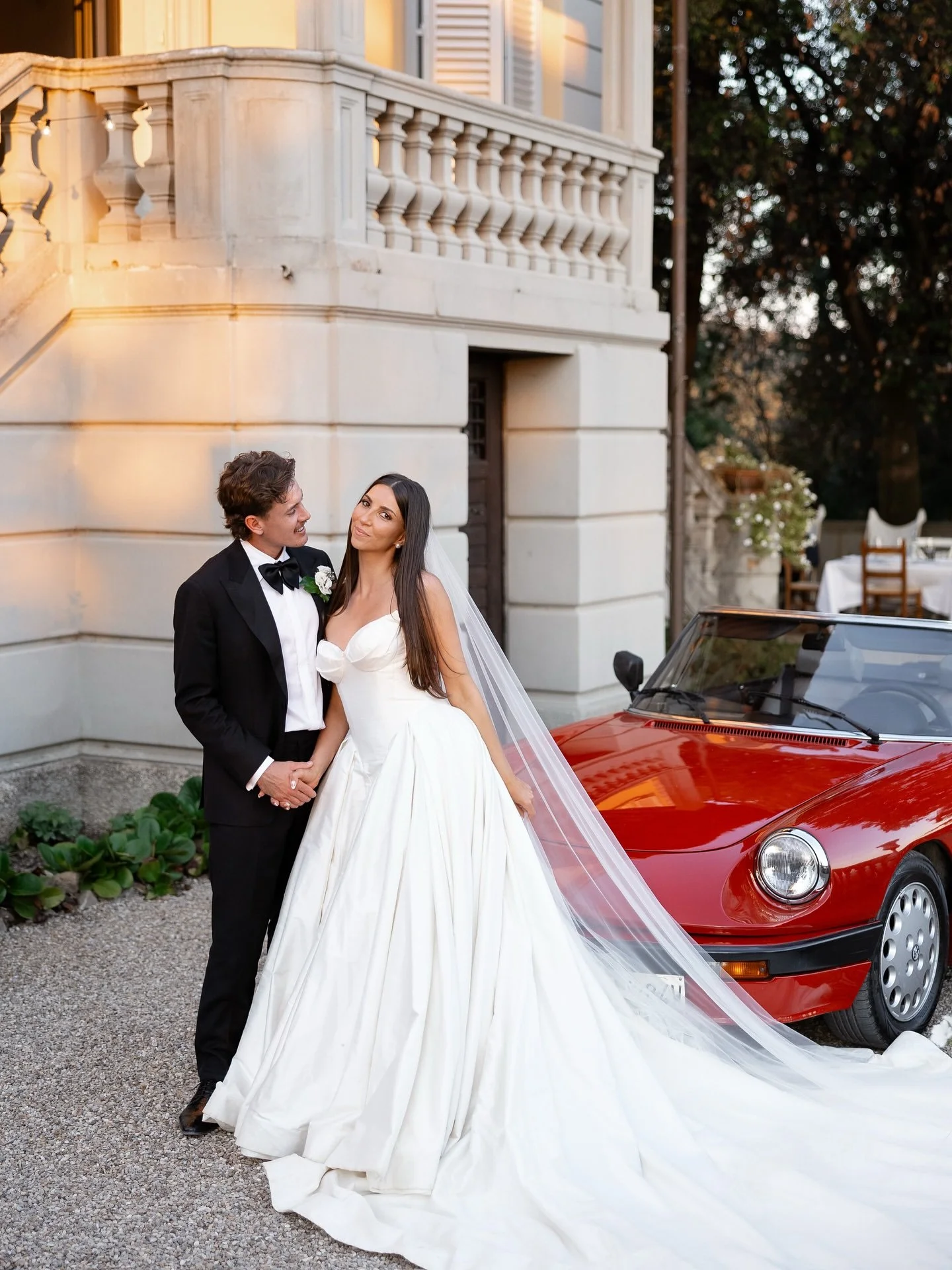 Bride and groom beside a red vintage car on the terrace at Villa Belvedere, Loro Ciuffenna