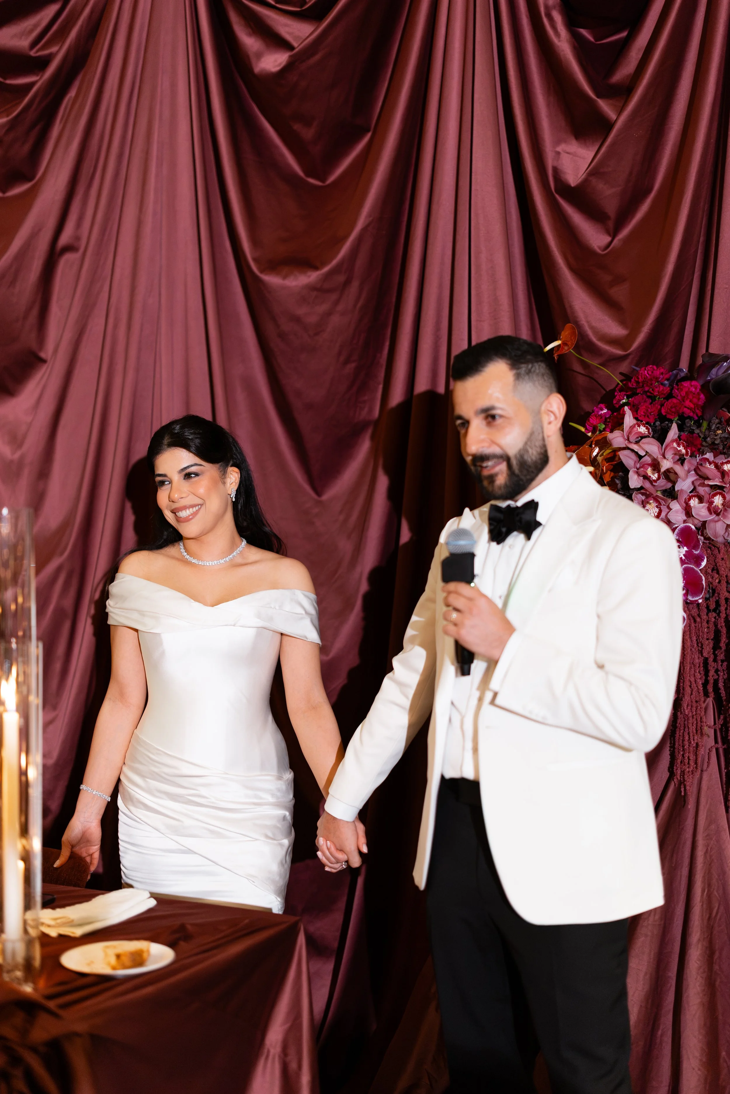 Jihan and Rob holding hands in front of burgundy silk drapes at Luci Melbourne