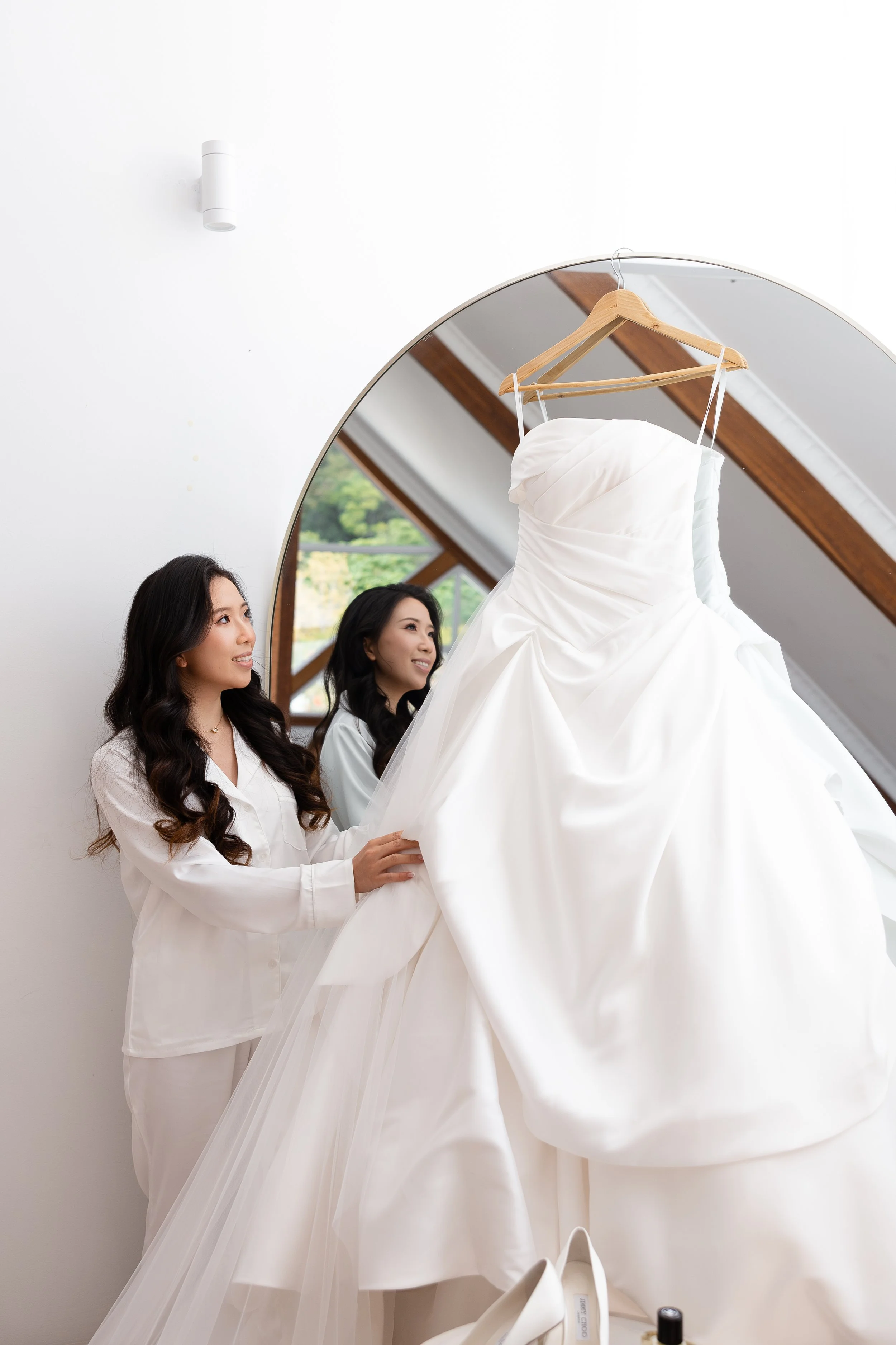 Alicia in a white robe beside her wedding gown hanging in front of an arched mirror
