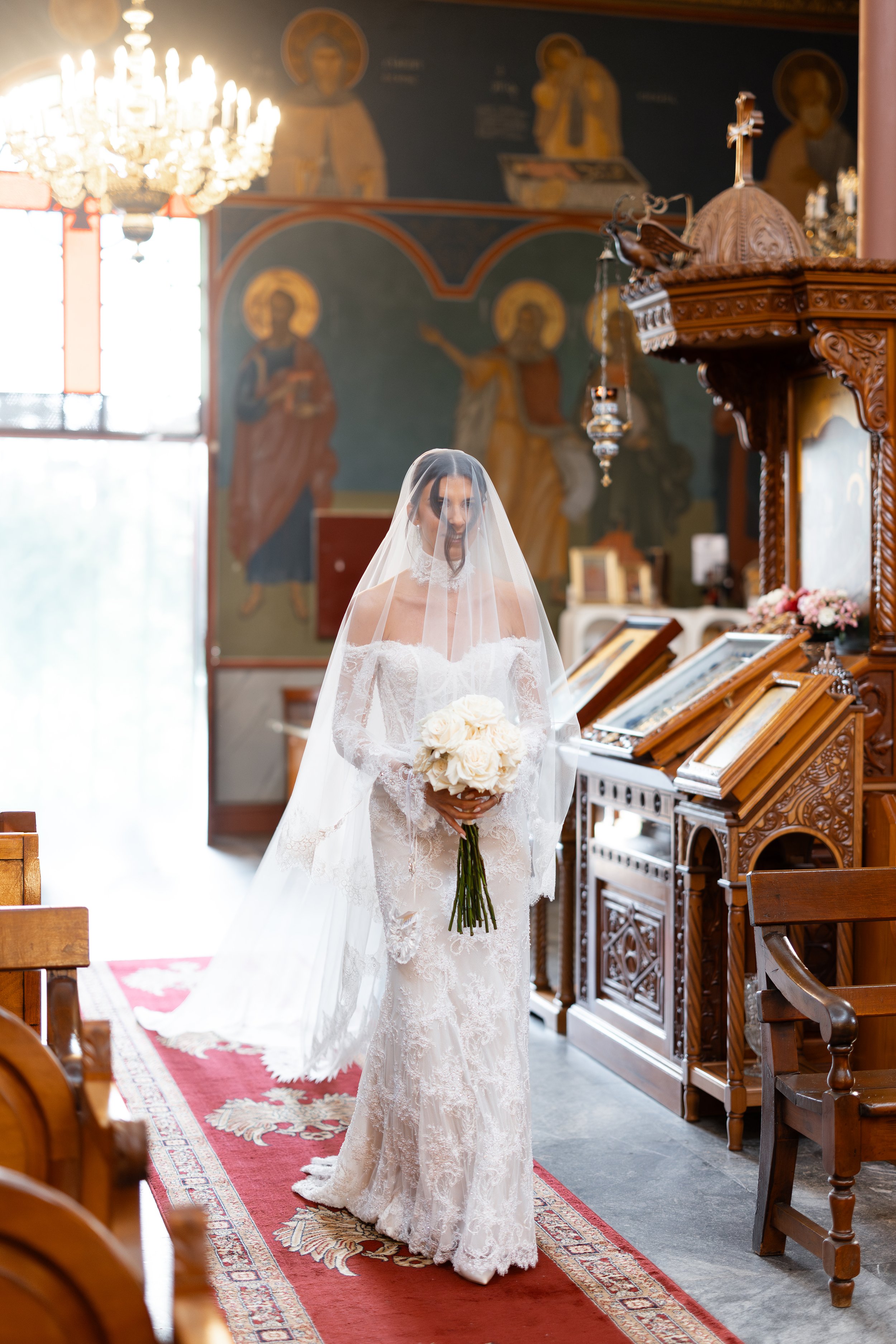 Steph in her veil holding a white bouquet beside an ornate lectern inside Holy Monastery of Panagia Kamariani
