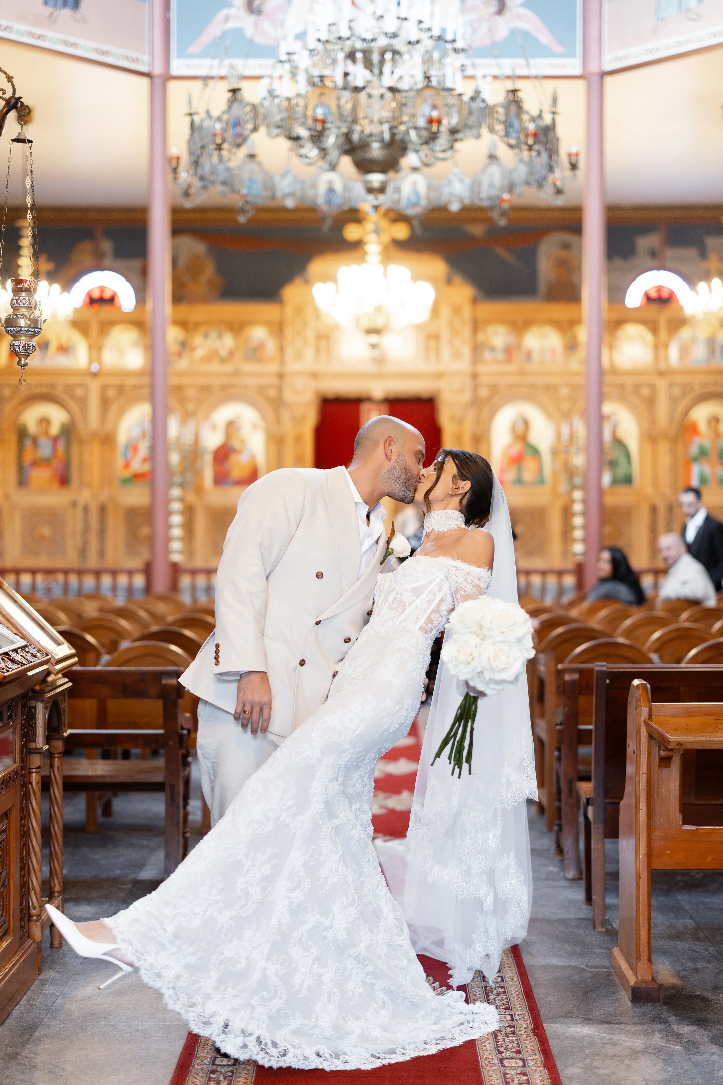 Steph and Alex kiss in the church aisle, Steph in her veil and lace gown