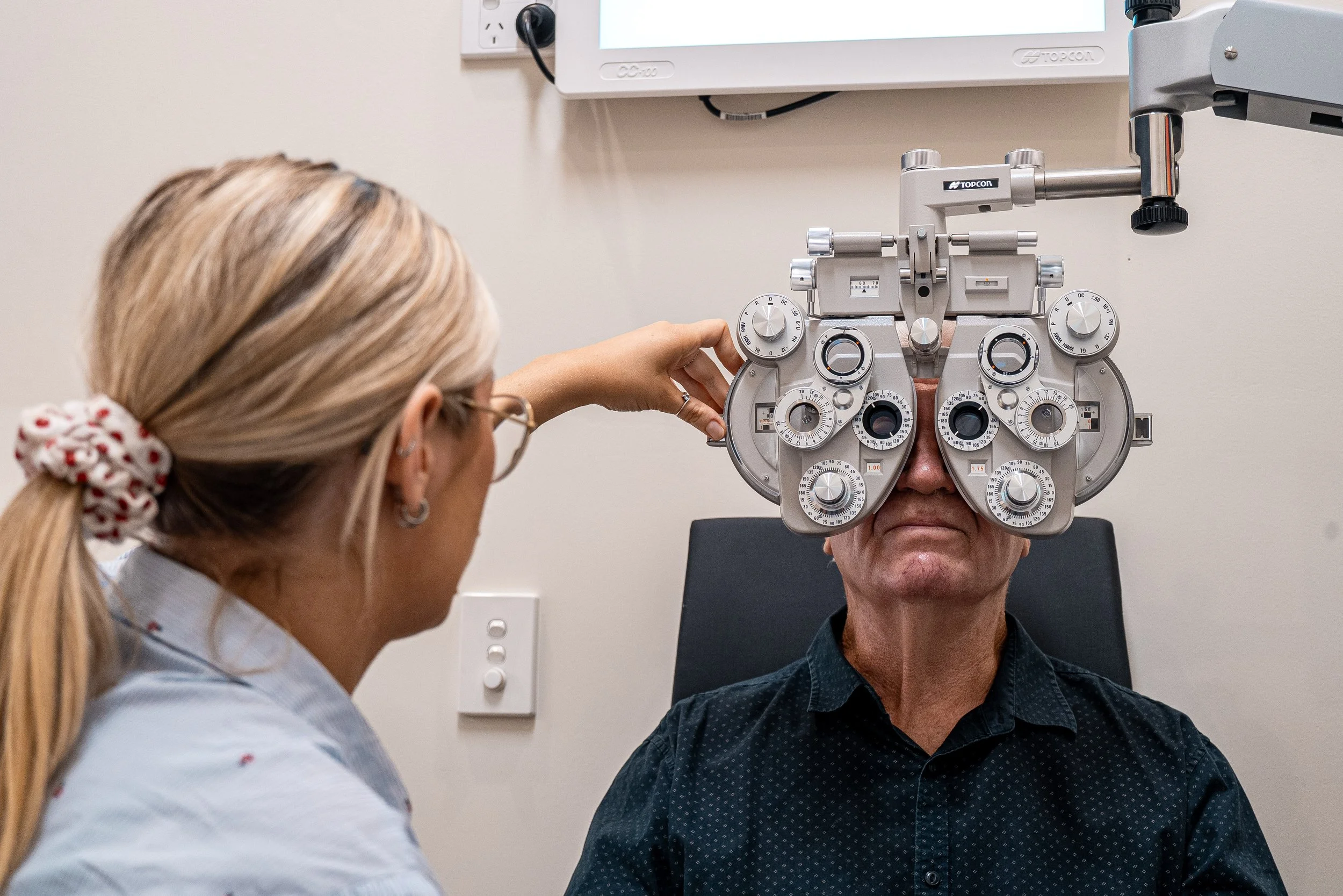 A healthcare professional adjusting a phoropter in front of a male patient during an eye examination.