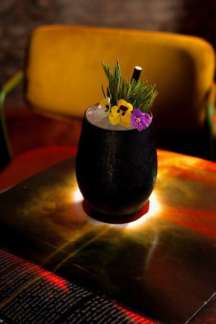 Cóctel Black Hole Sun en vaso negro con flores comestibles, en Standard Soho, Málaga