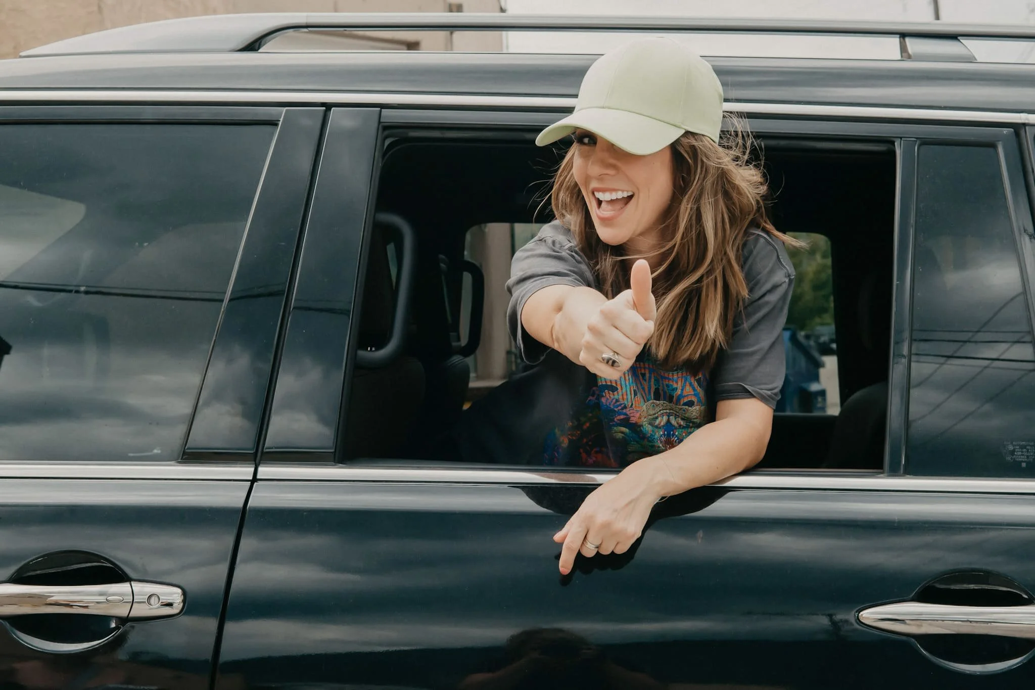 Graphic designer Jodi, giving a thumbs up while leaning out of car window.