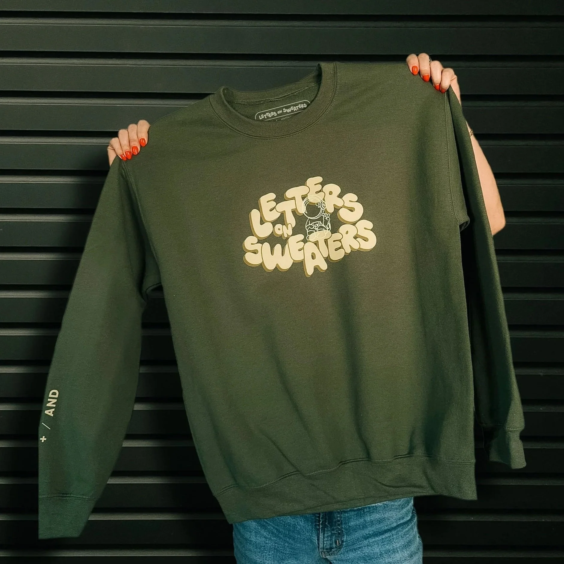 Holding military green crewneck sweatshirt with bubble letters and moon man design