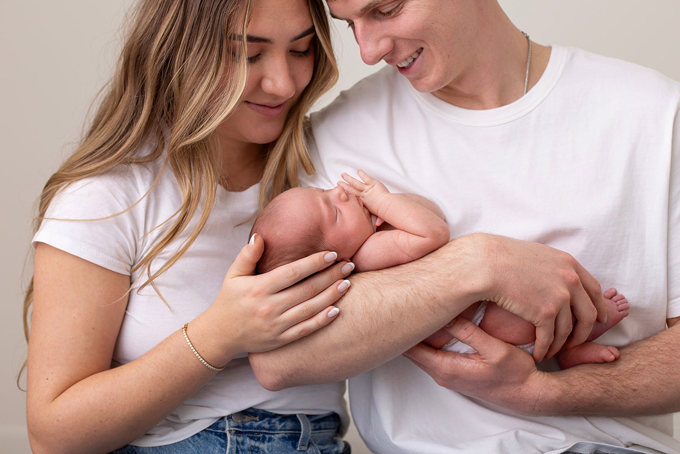 young parents smiling, looking down, and holding their newborn baby