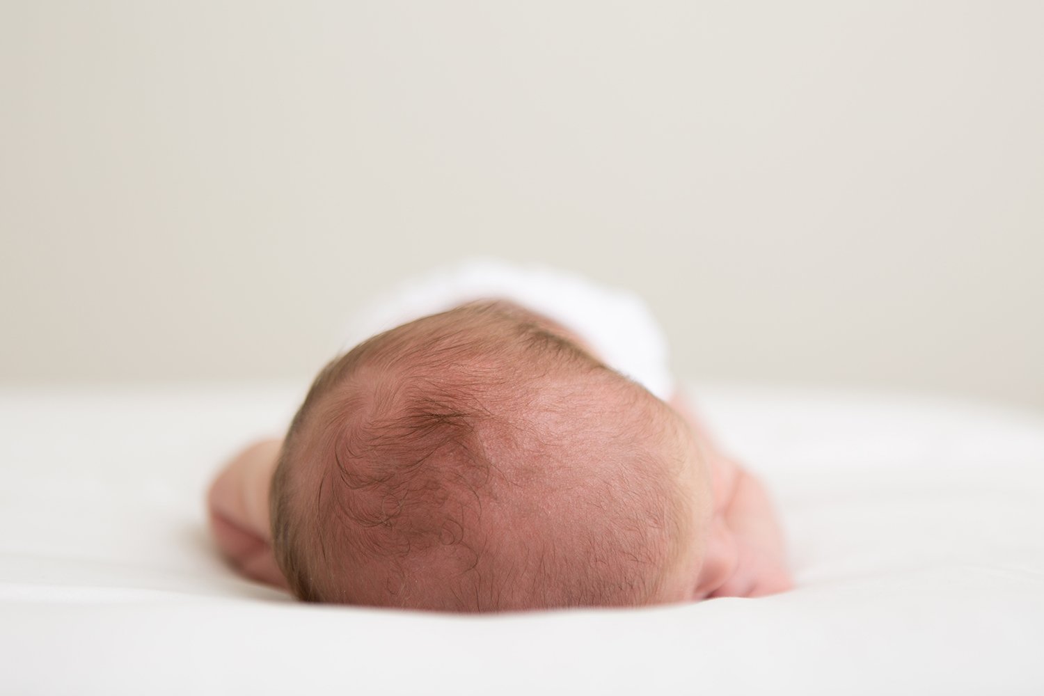 Newborn baby lying on their tummy on a white studio blanket, photographed in soft light