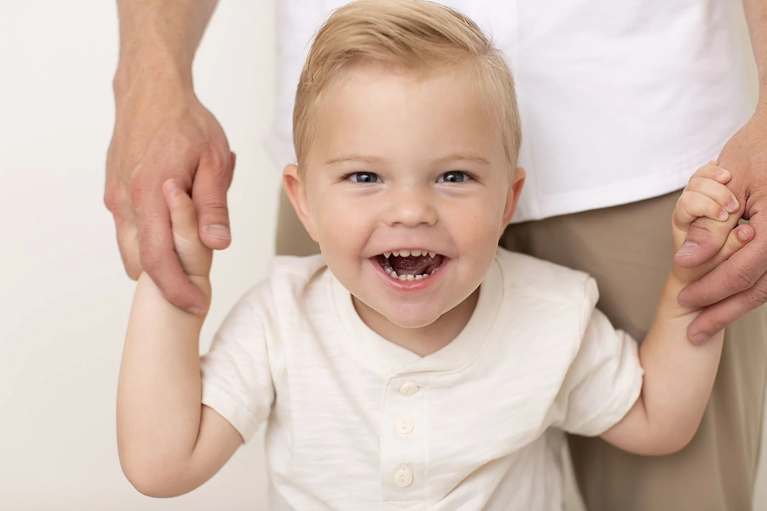Studio portrait of a smiling toddler holding parents’ hands, photographed by a Utah County children’s photographer