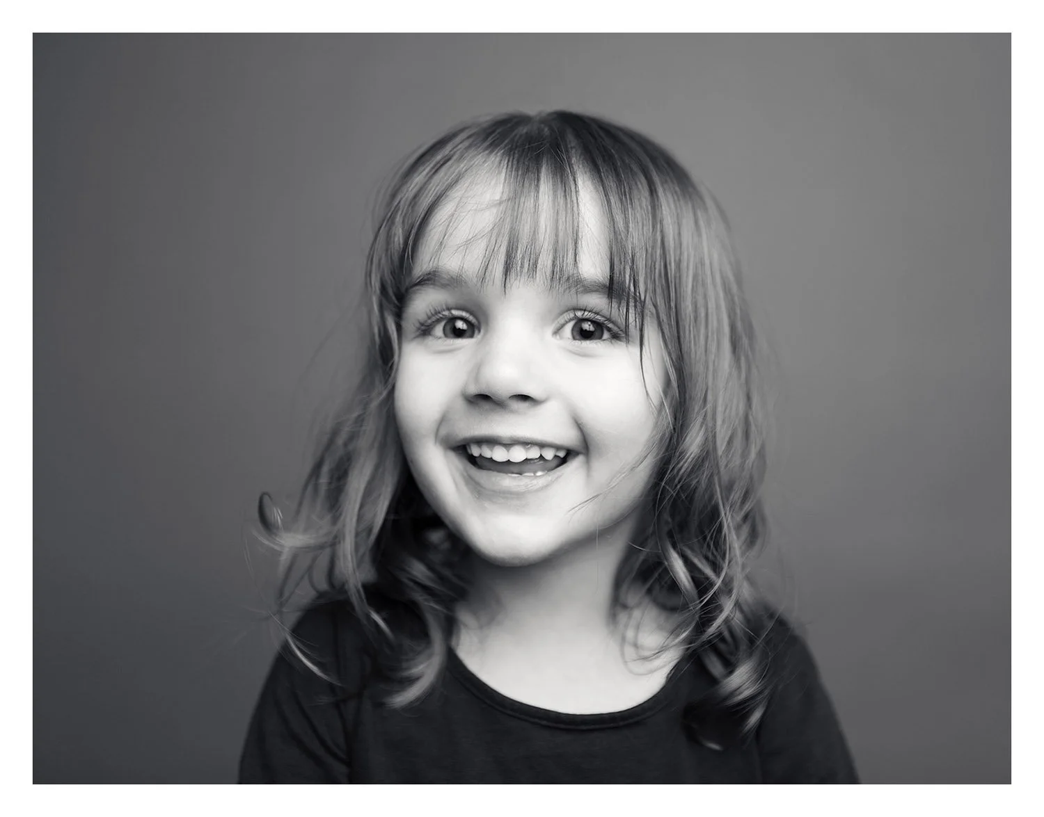 Black and white studio portrait of a smiling toddler girl with bangs, photographed by a Utah County children’s photographer