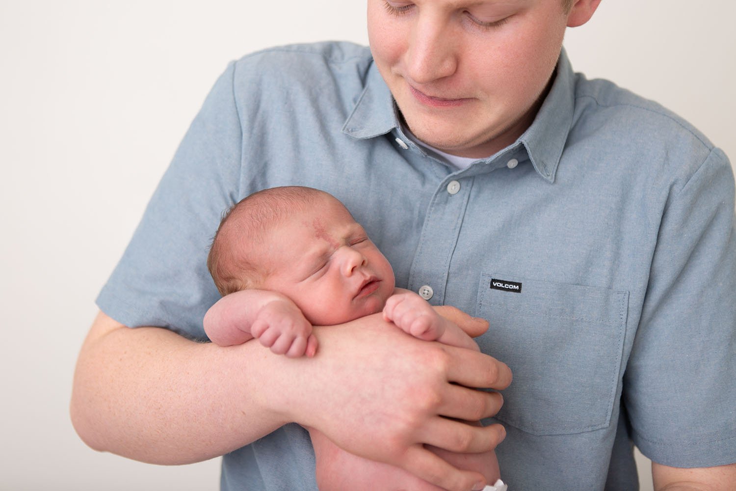 Father holding his newborn baby during a natural, baby-led posing newborn photography session in a Utah County studio
