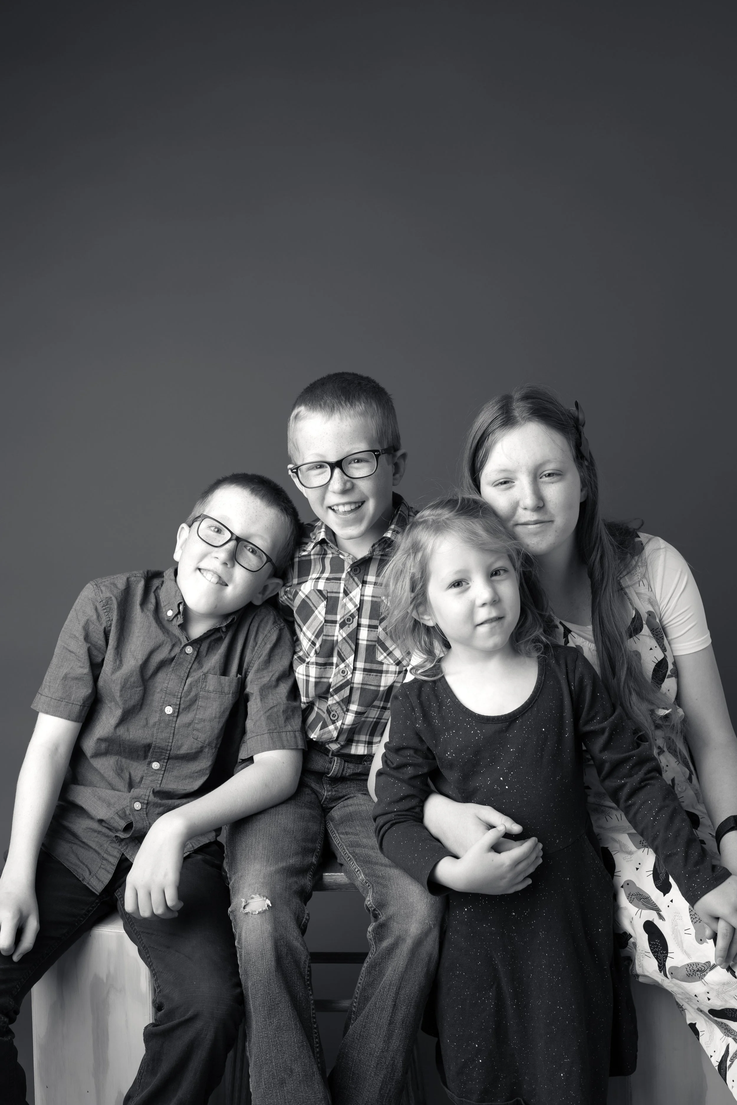 Black and white studio portrait of four siblings sitting together.