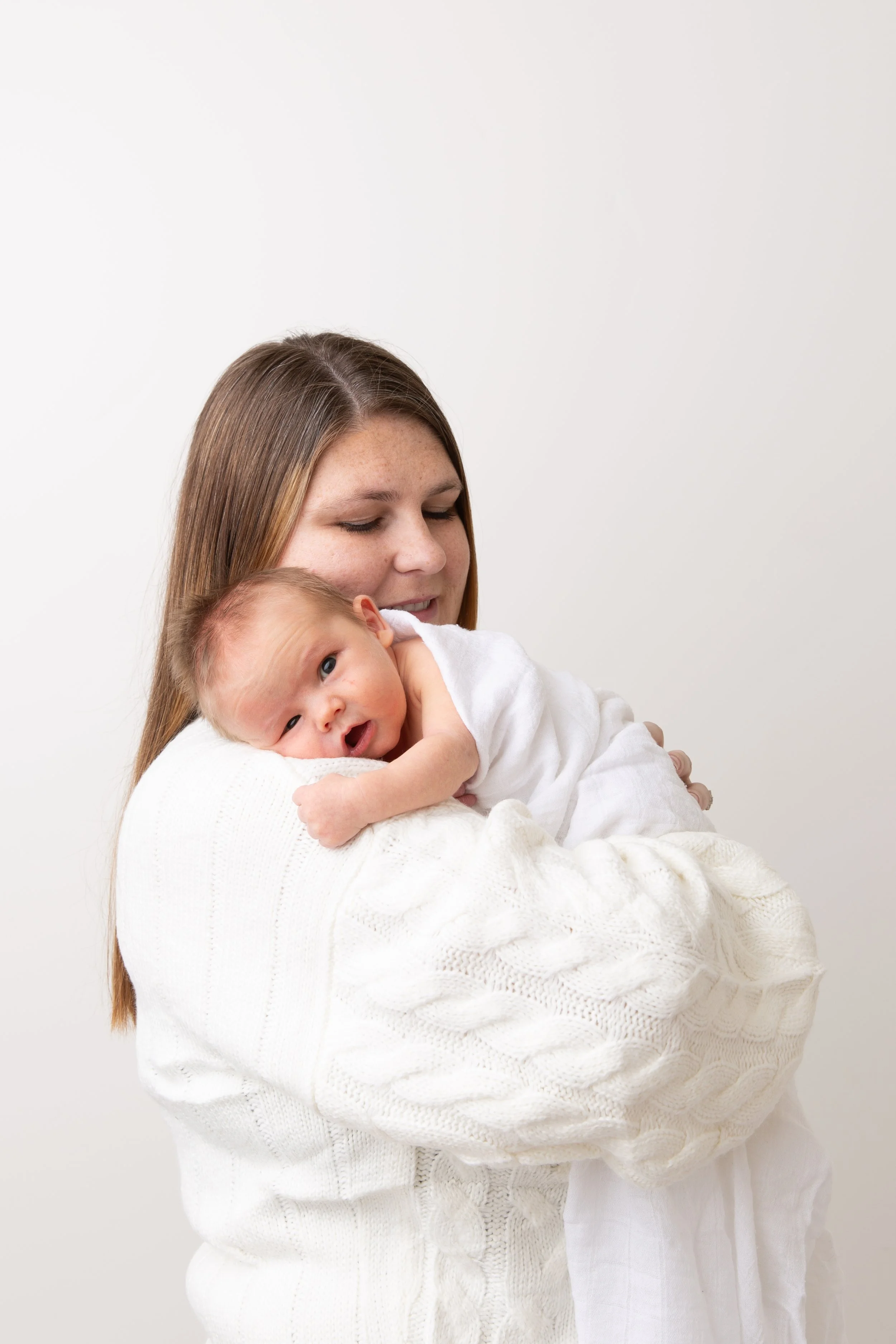 Mother holding newborn baby against her shoulder during a soft light studio session by a Utah County newborn photographer.