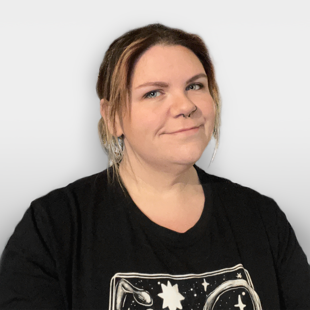 A smiling woman with light brown hair, light skin, wearing a black top, and a nose piercing, against a plain white background.