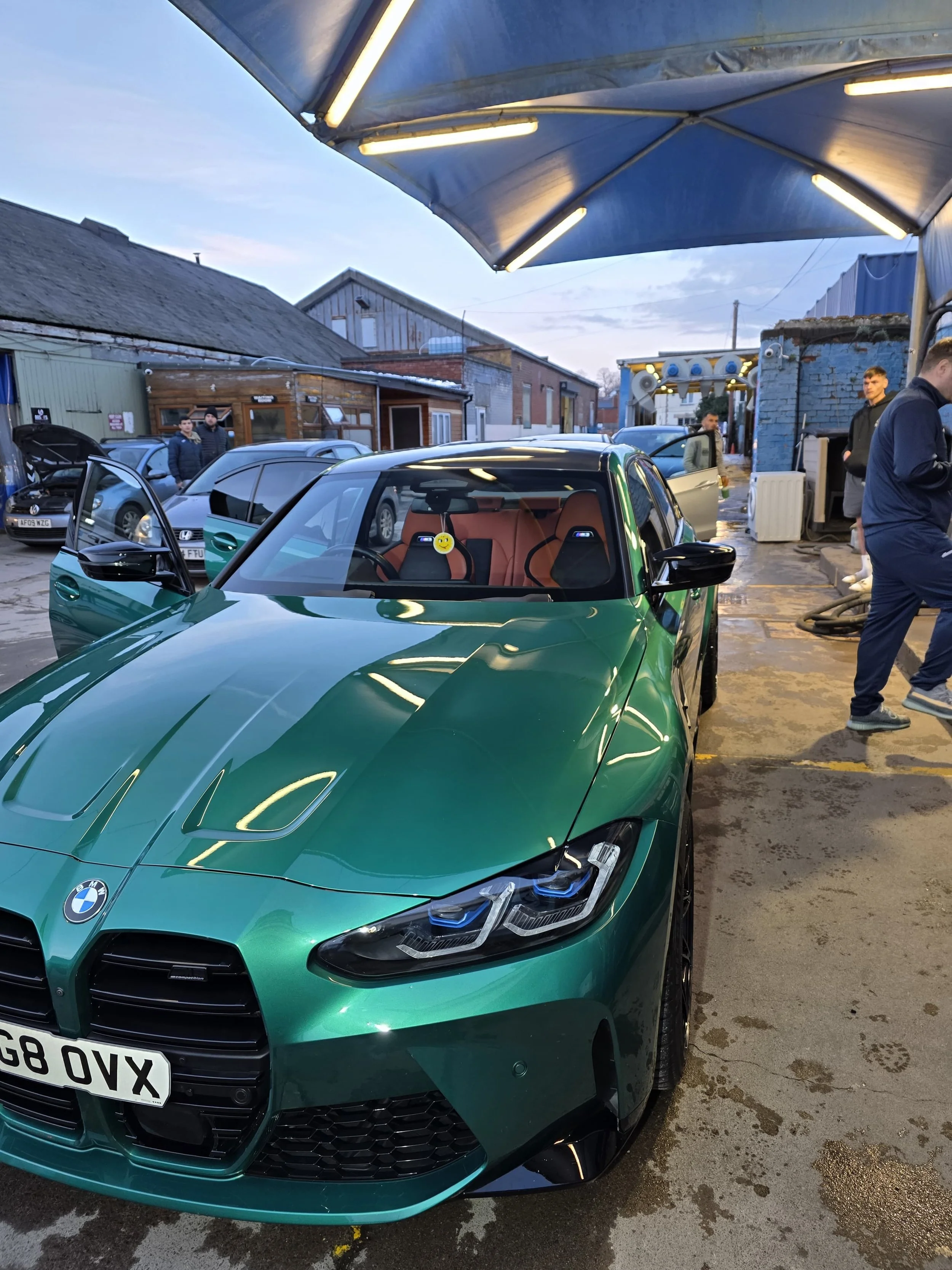 A green BMW car with a black grille and license plate G8 OVX parked at a car wash or detailing shop with people in the background.