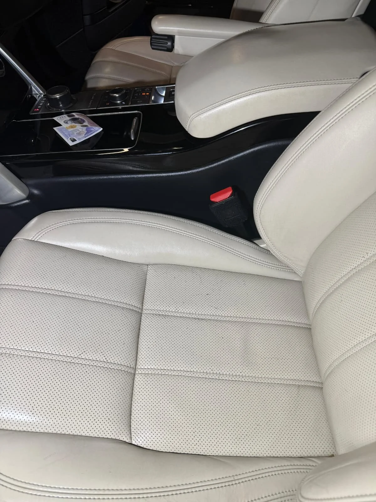 The interior of a car showing the front passenger seat, center console with controls, and part of the driver's seat, all in light beige leather.