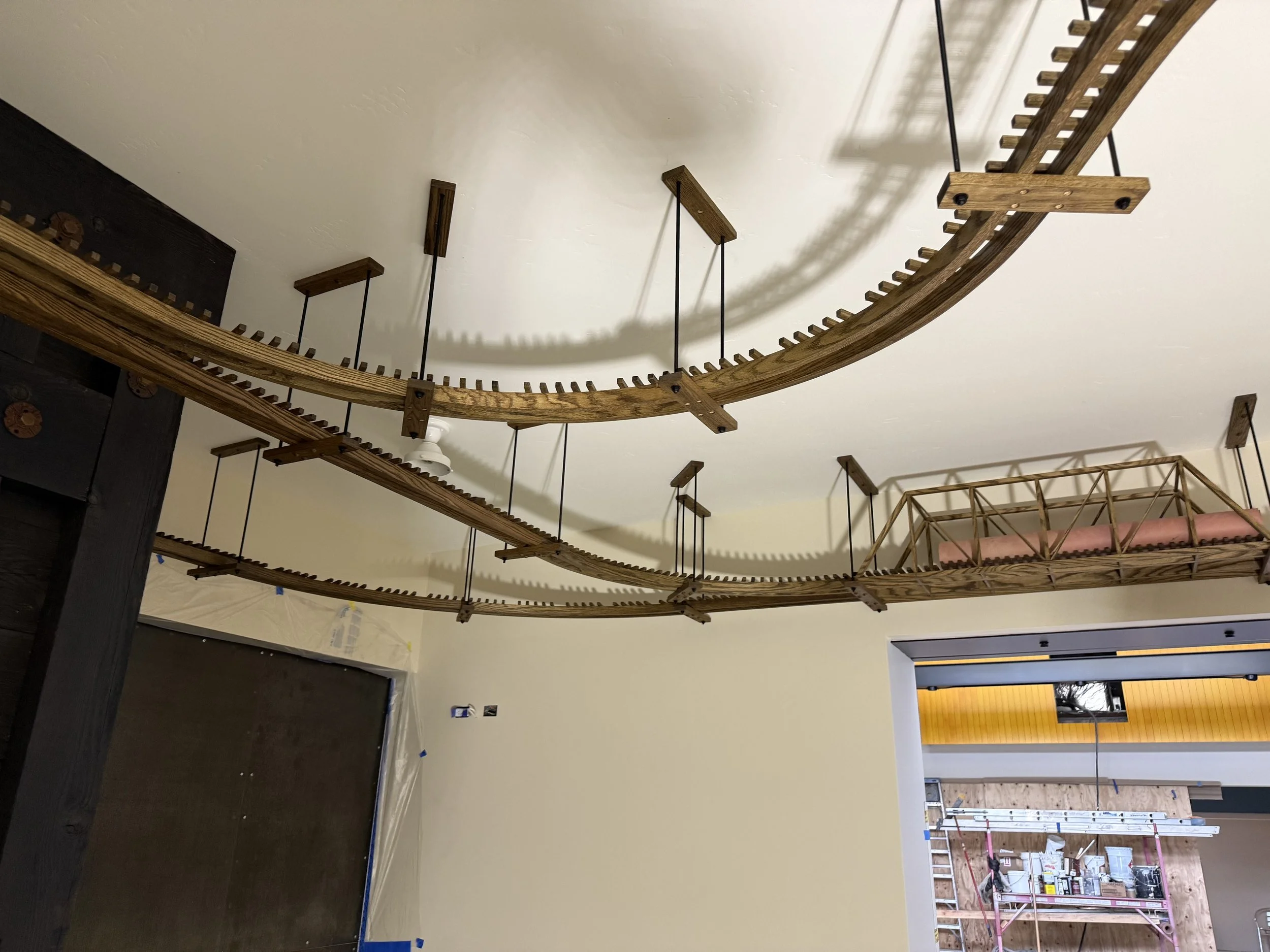  Wide view looking up at two curved overhead track runs suspended from the ceiling on hanger rods, with a truss bridge section visible in the background. 