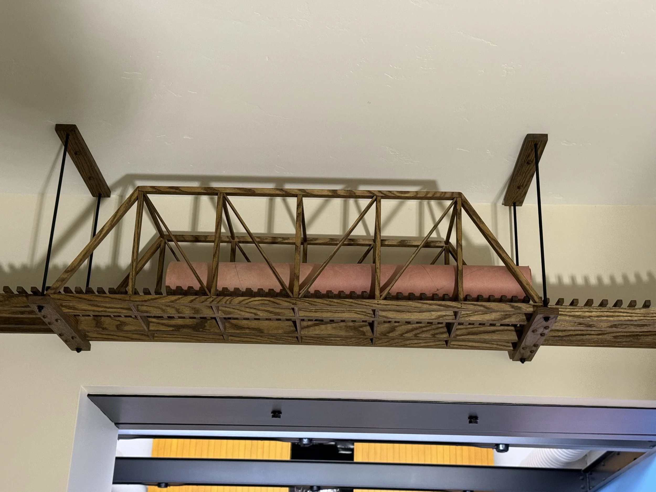  Close-up of a wood-truss bridge section on the overhead track, with a padded/wrapped protective sleeve around a beam running through it. 