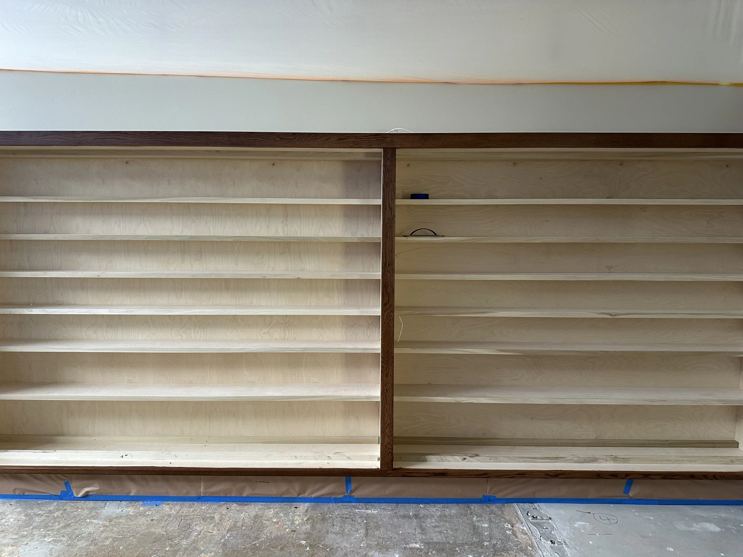  Close-up of finished built-in shelving units — light plywood shelves framed in dark stained wood, still empty. 