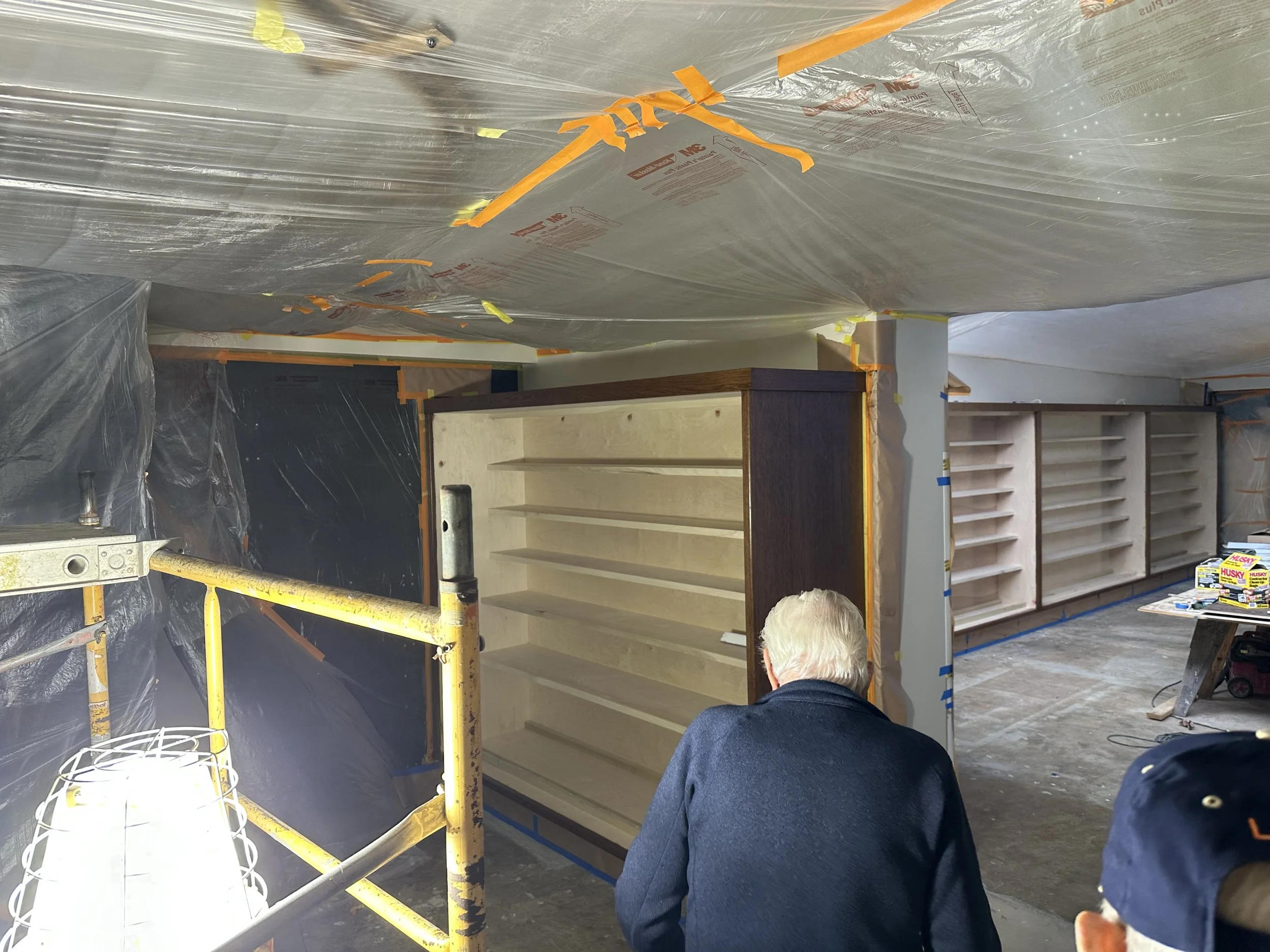  Wide interior shot: Museum Staff examine a shelving unit under construction, with more finished shelving runs visible down the hall. 
