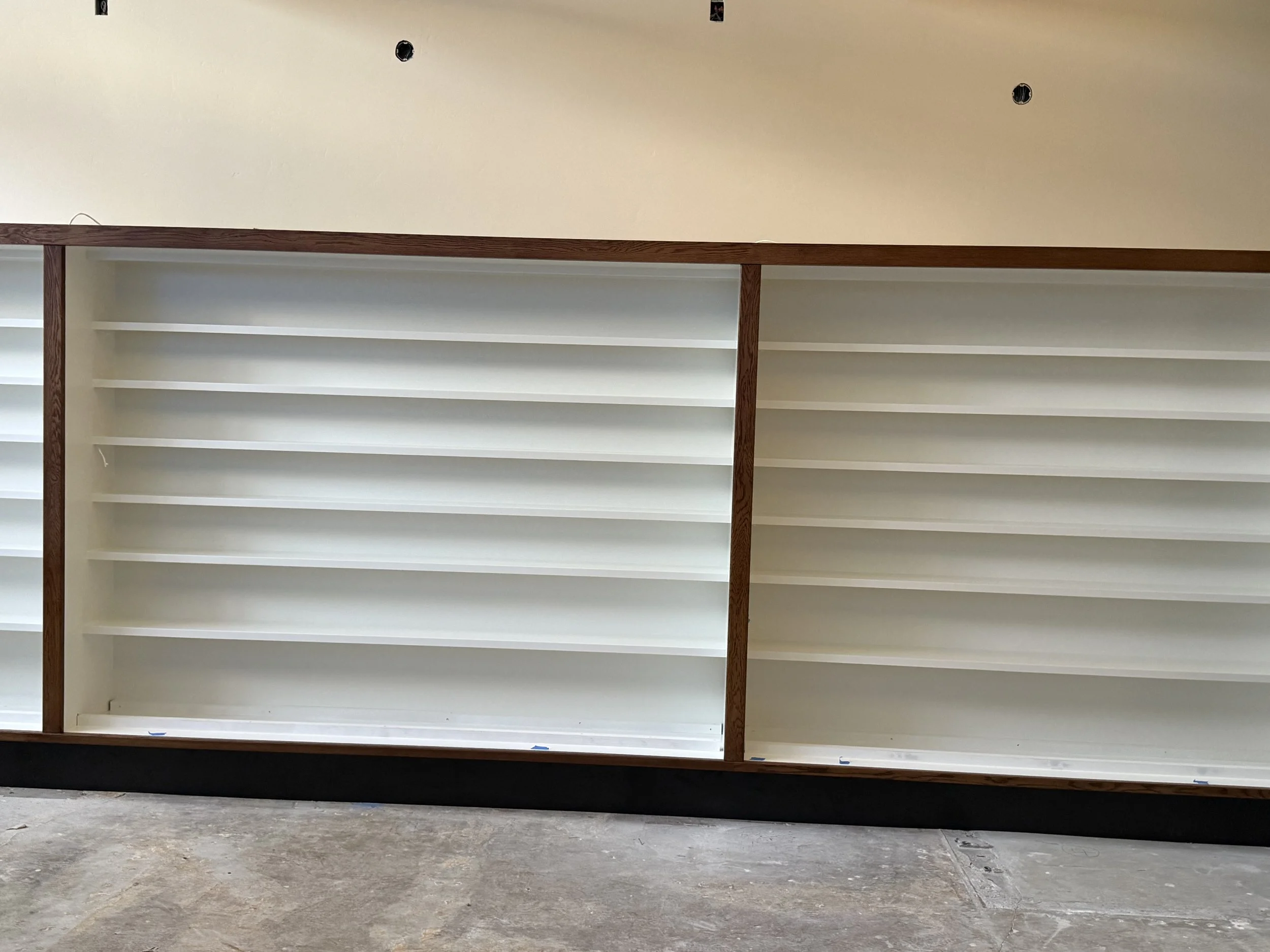  Two adjacent shelving bays, white-painted shelves framed in dark wood trim, spanning a long wall. 