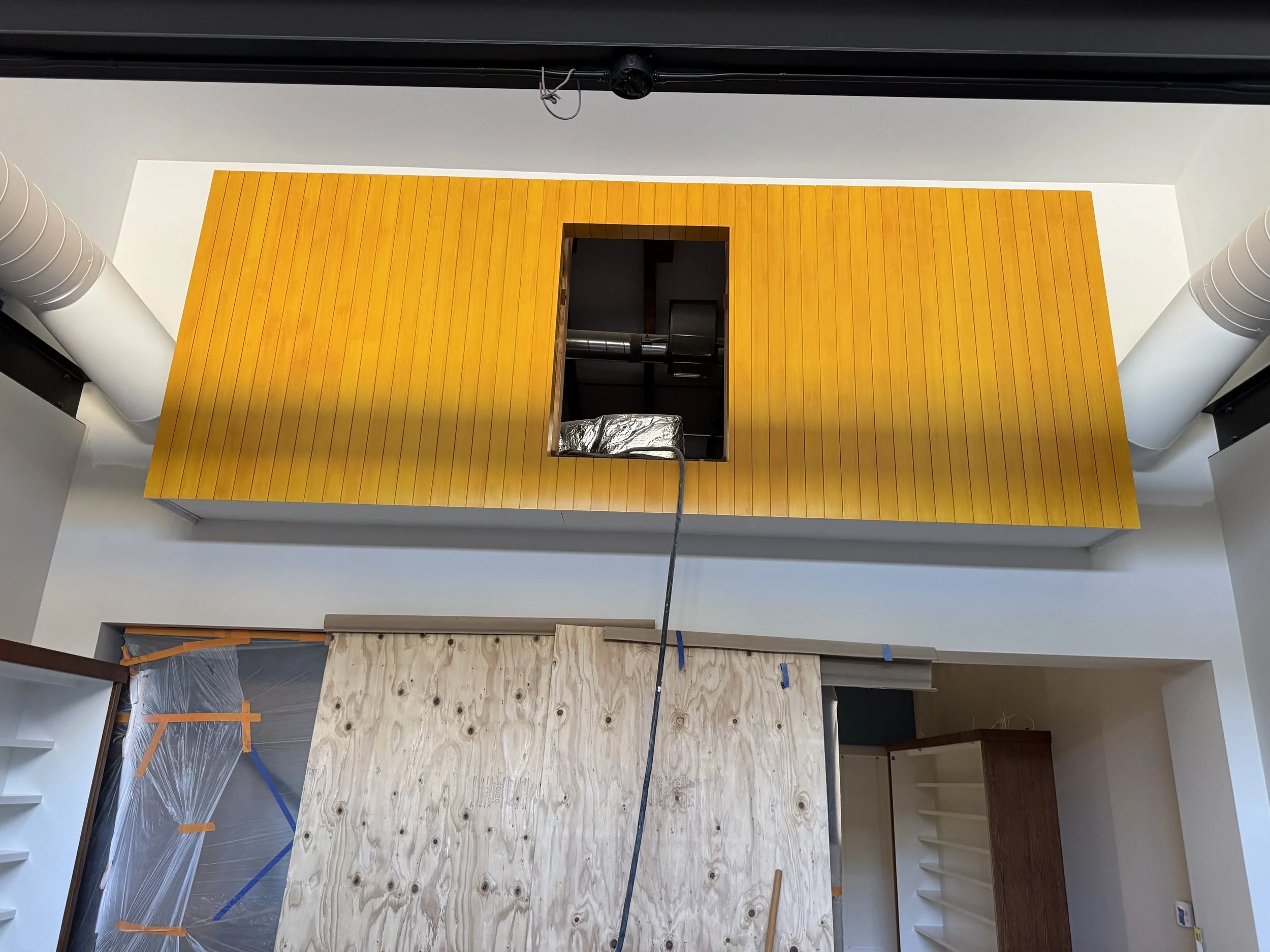  Close-up of the finished boxcar enclosure in mustard-yellow wood cladding, with its access panel open showing ductwork inside. 