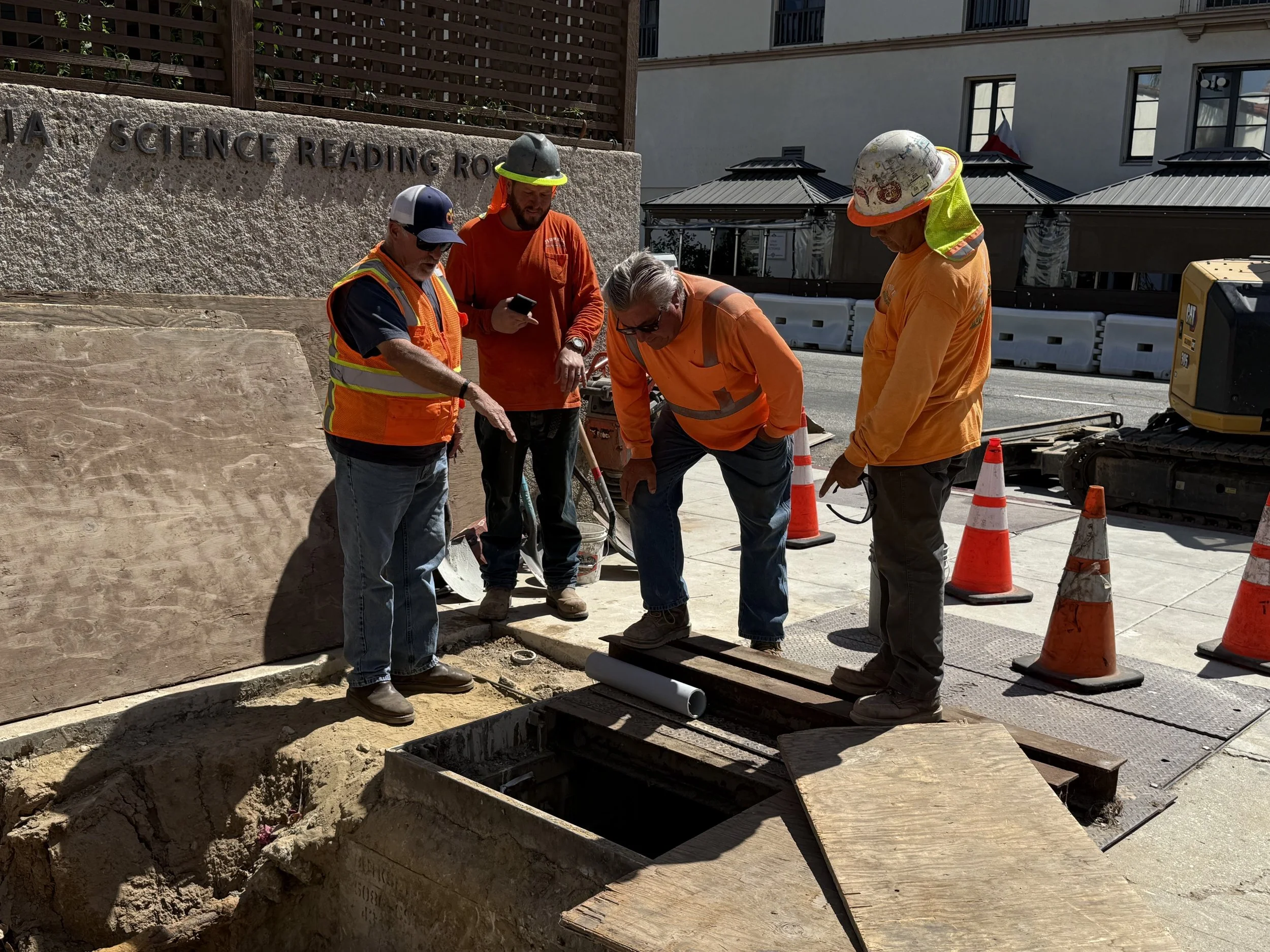  Four crew members gathered around an open underground vault, looking down at conduit being run into it. 