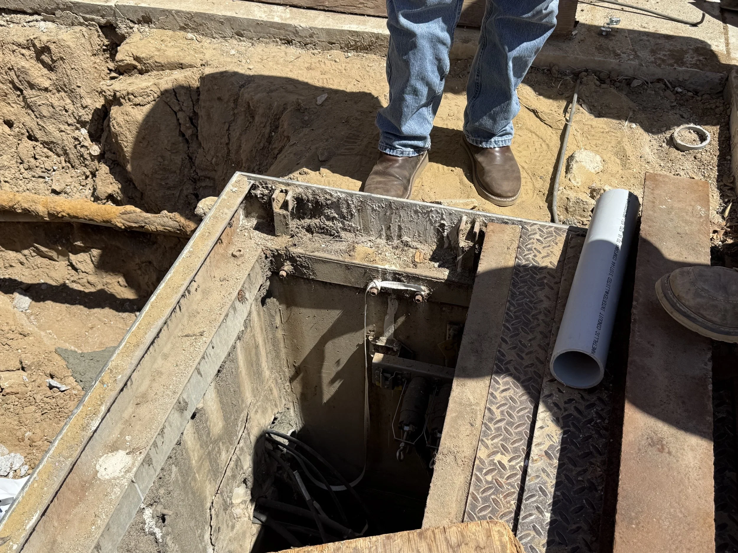  Close-up looking down into the vault: electrical conduit, wiring, and a length of PVC pipe being fed in. 