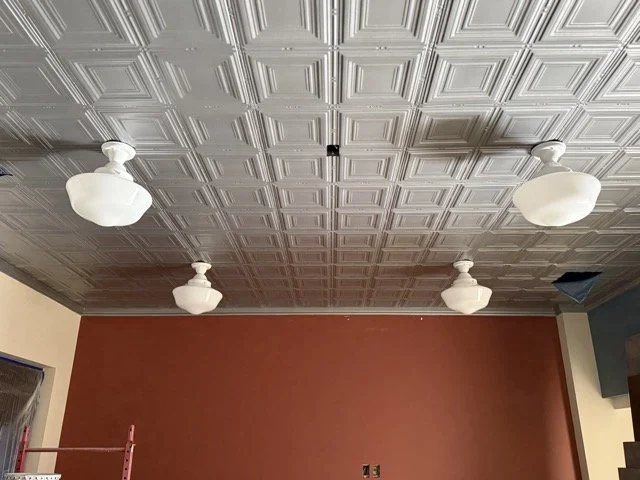  The lounge: pressed-tin ceiling panels with four white schoolhouse globe lights installed above the terracotta wall. 