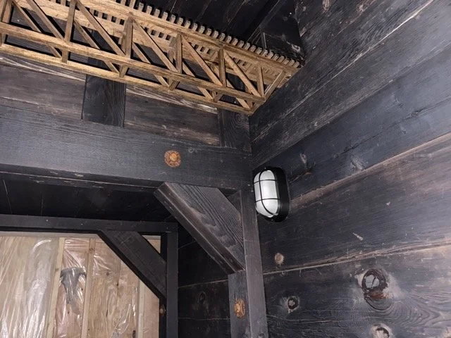  The tunnel: dark timber walls and beams with an oval caged wall light, and the wooden truss model overhead. 
