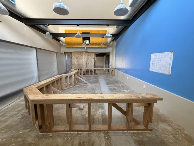  Head-on view of the framed base, with the pendant lights and black steel beams overhead and plastic sheeting protecting the left wall. 