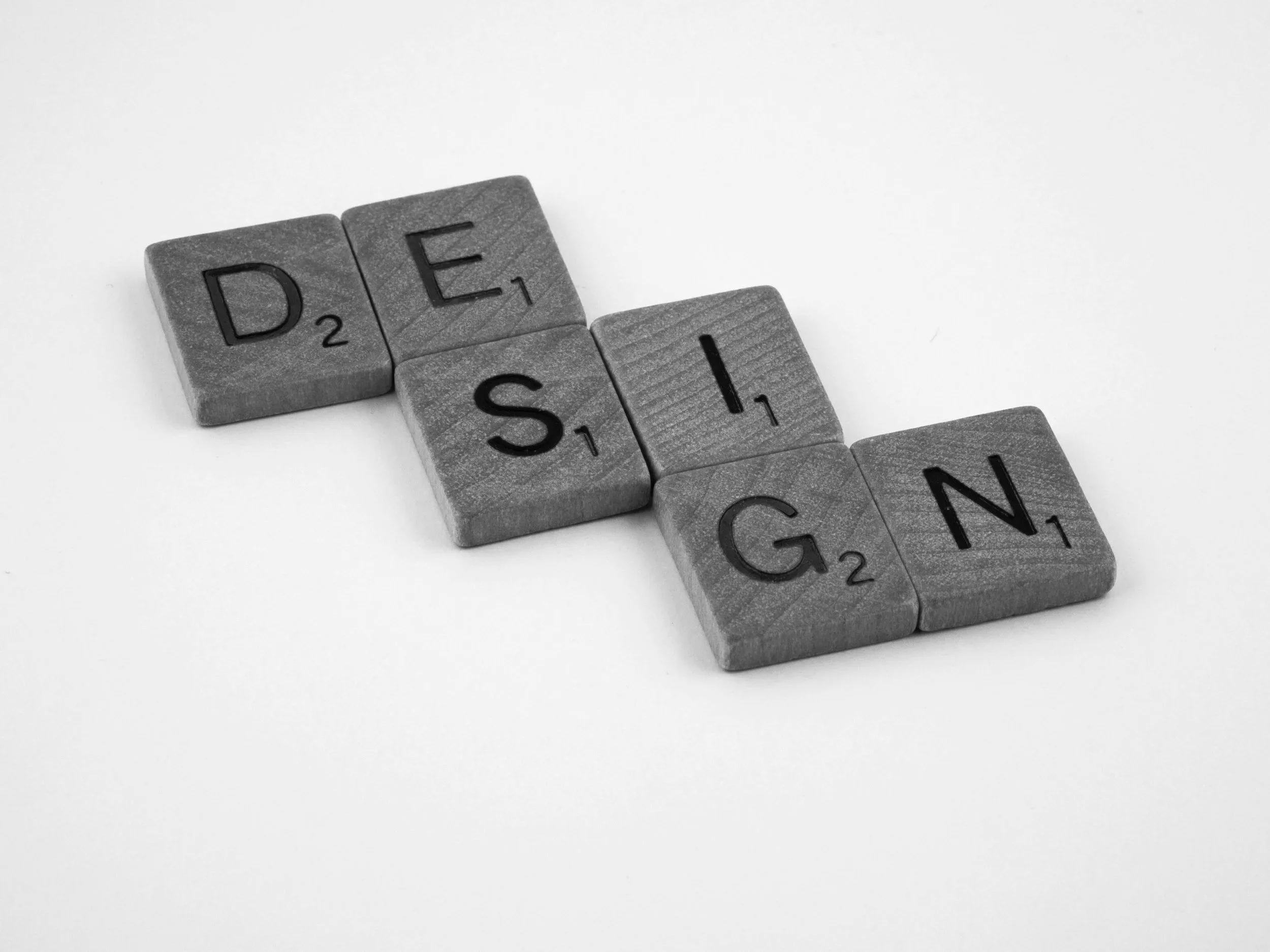 Black and white photo of individual Scrabble tiles spelling 'DESIGN' on a white background.
