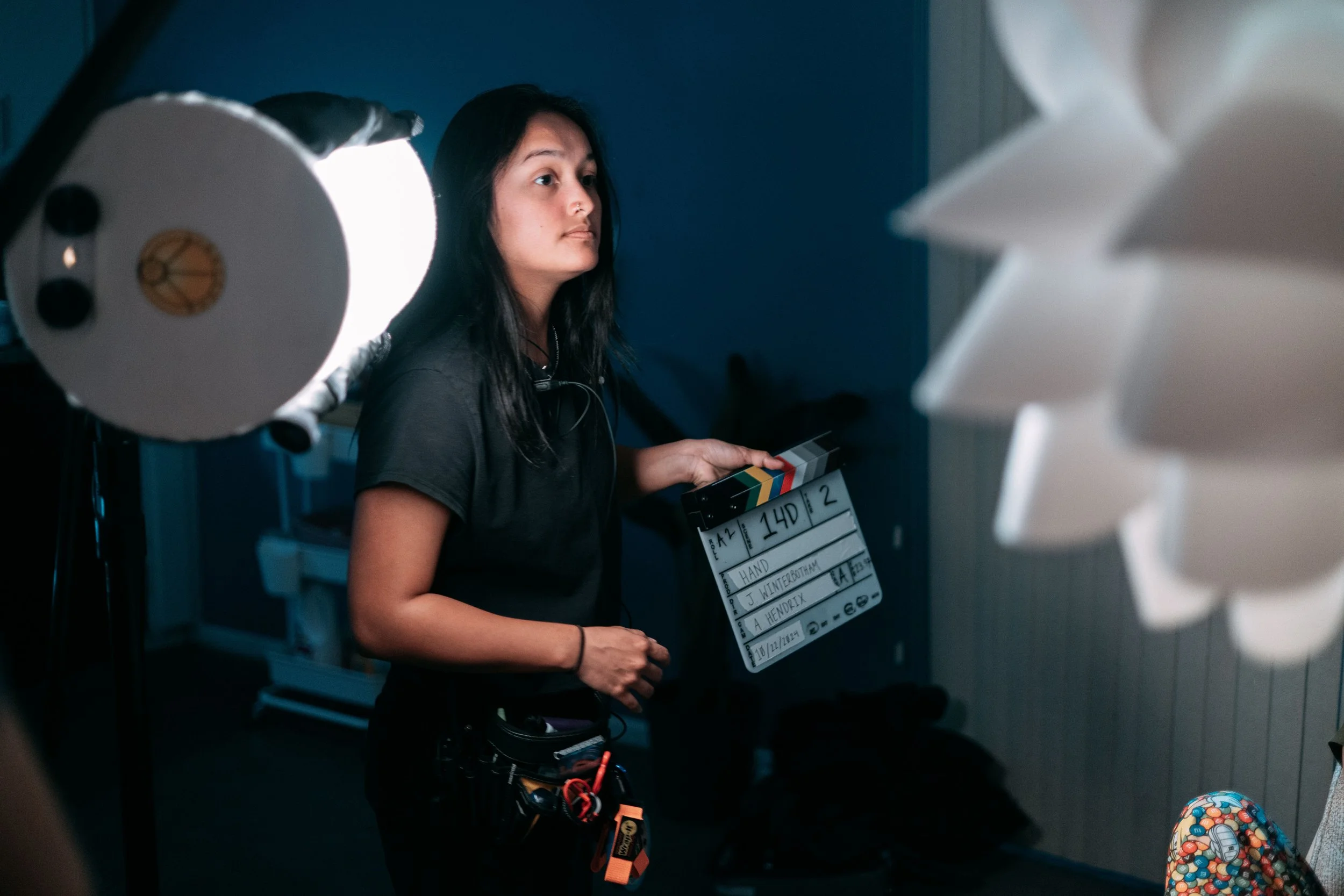 A woman using a director's clapboard on a film set, surrounded by professional lighting equipment.