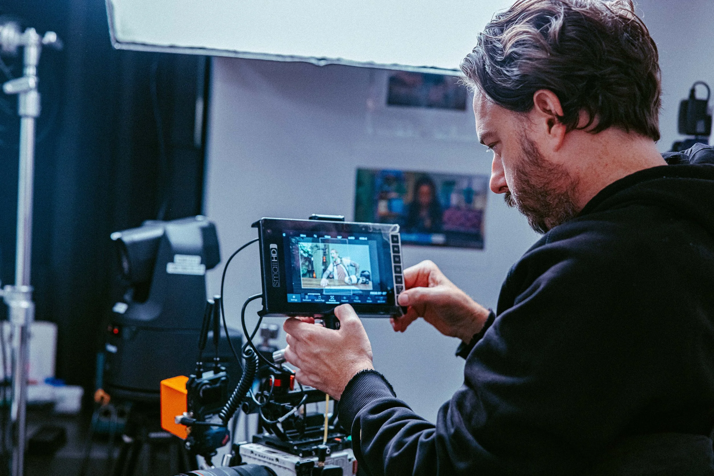 Man operating camera equipment on a filming set, with a monitor displaying a scene.