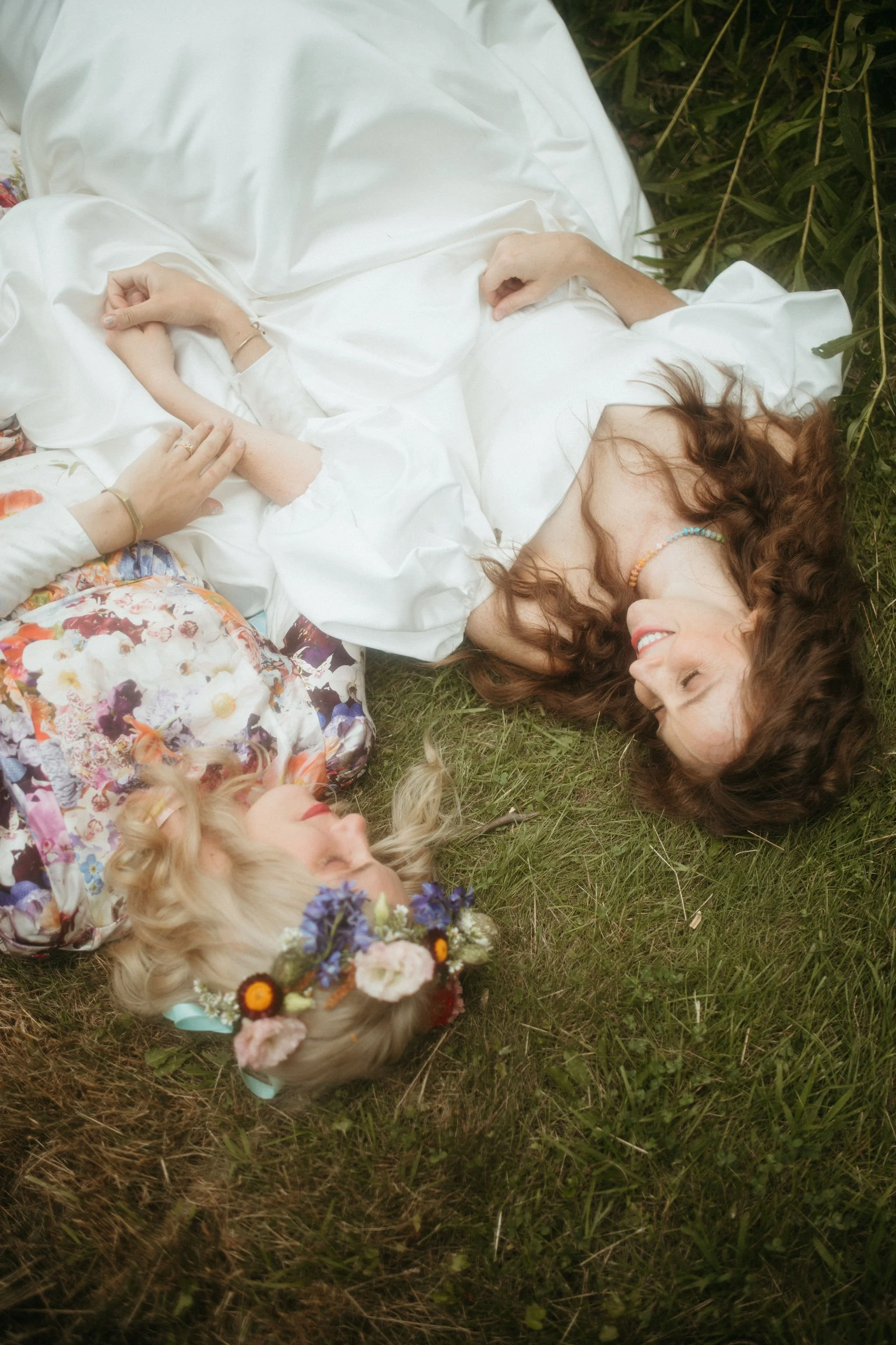 Two brides laying together in the grass in their wedding dresses in New York