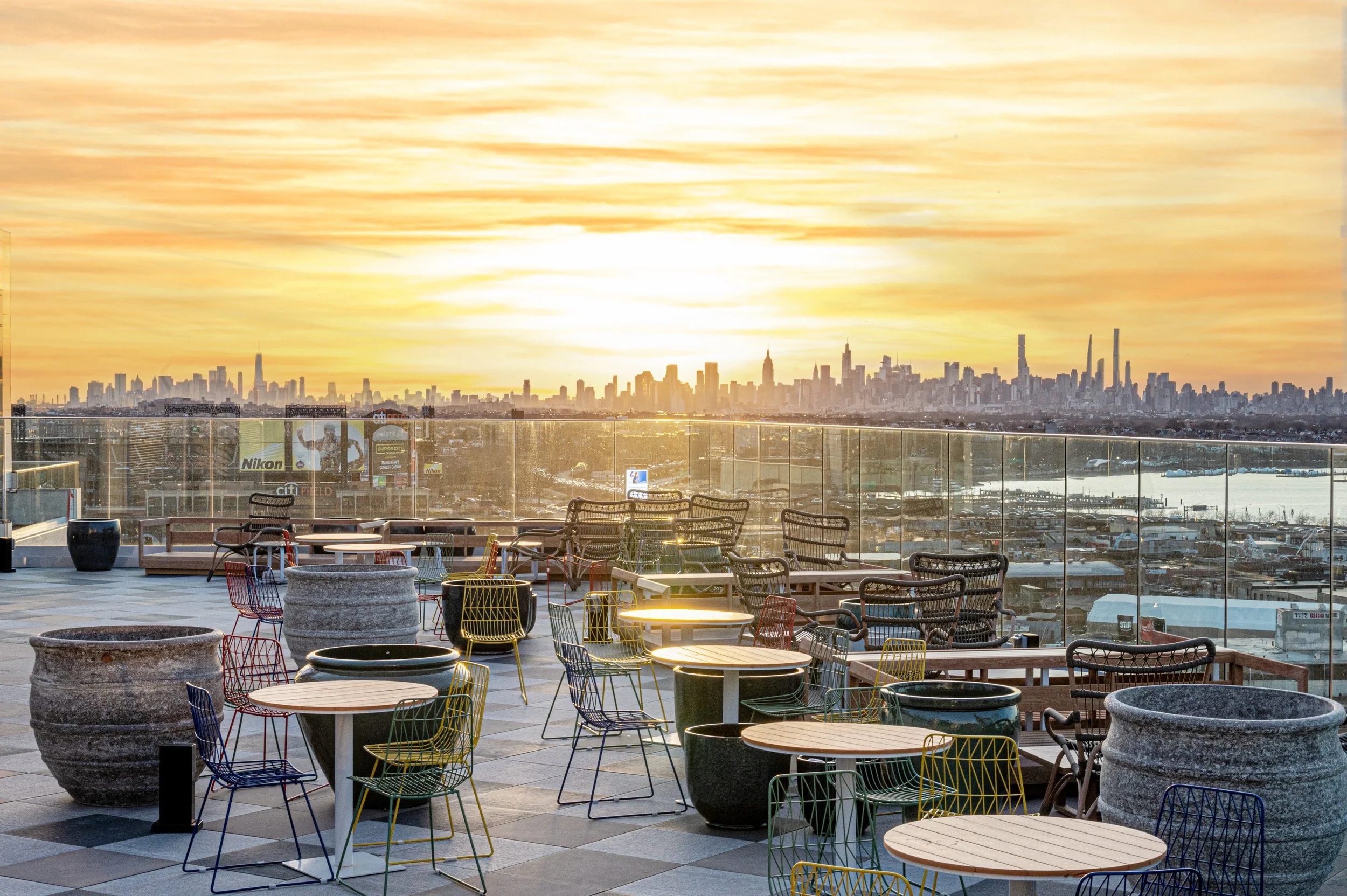 Rooftop patio with colorful chairs and tables overlooking a city skyline at sunset.